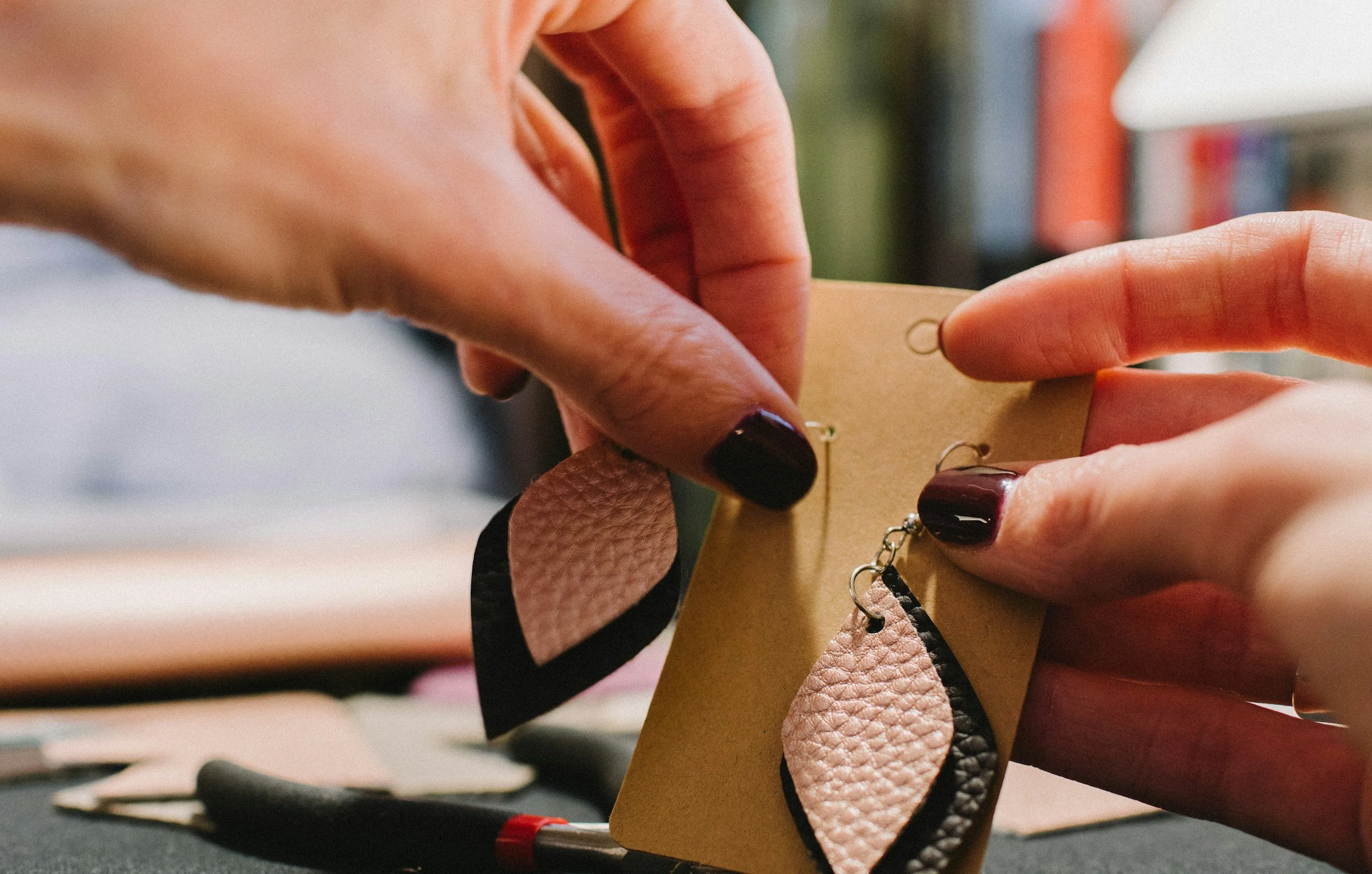 Person attaching earrings made of textured beige and black leather to a display card