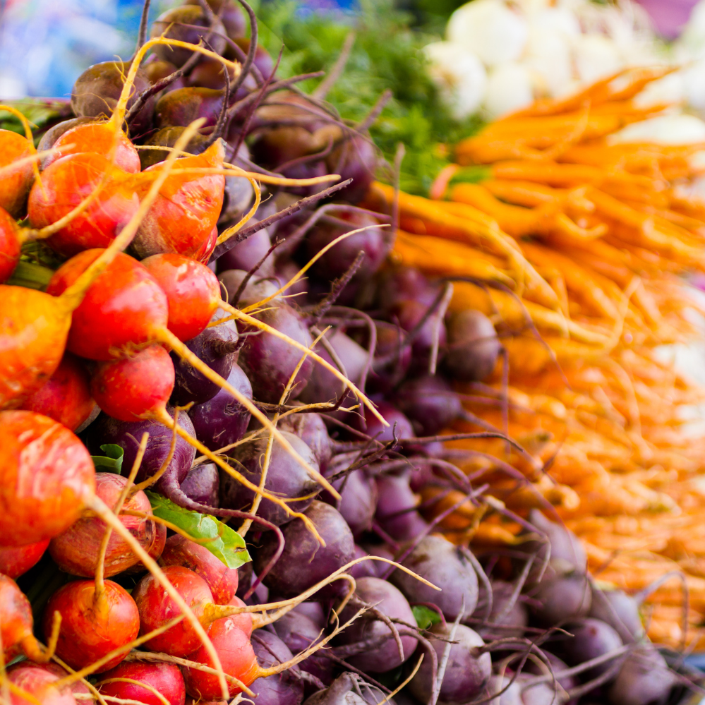 Colorful bunches of fresh radishes in red, purple, and orange, displayed at a market stall.