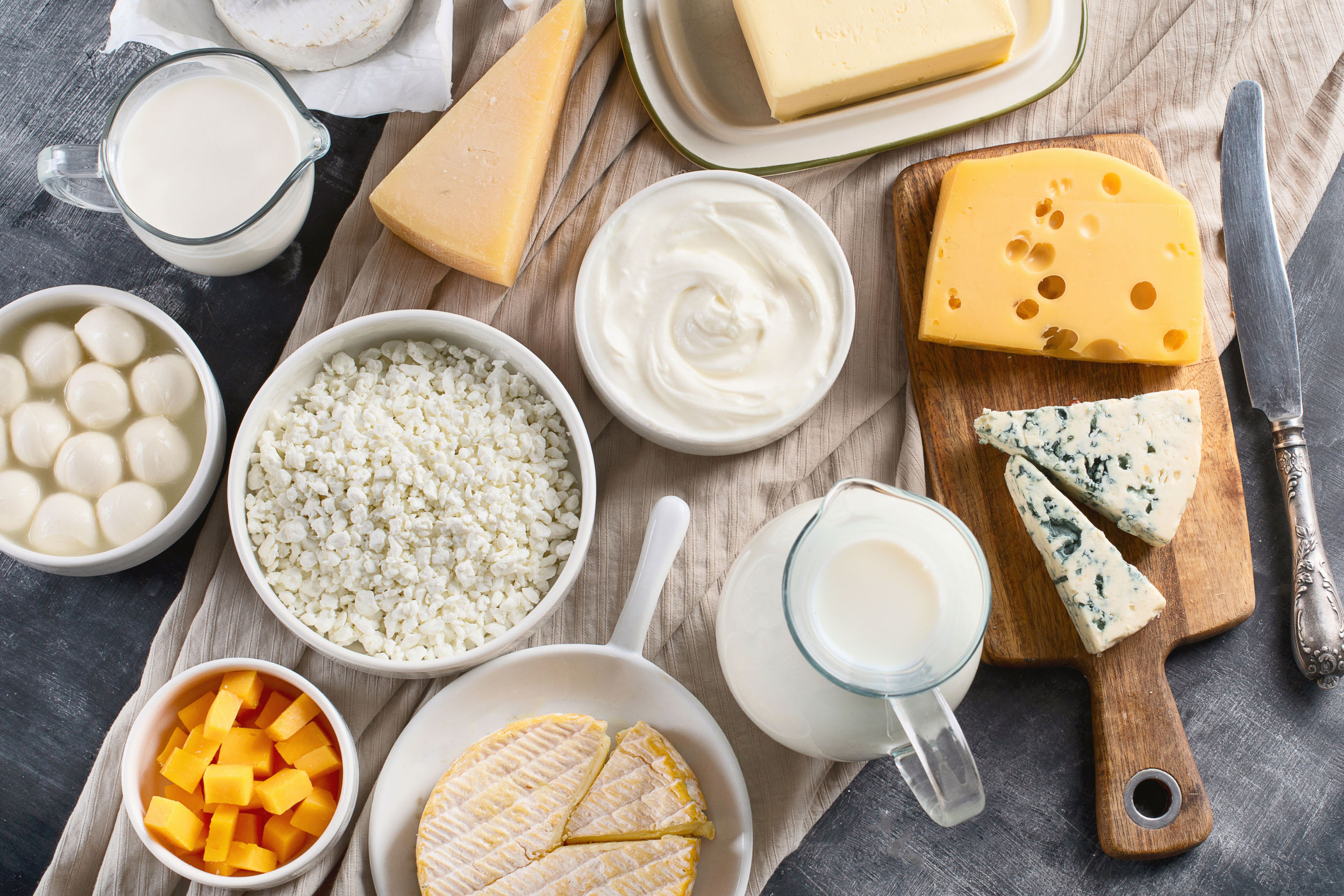 A variety of cheeses, milk, and dairy items on a table, including cheddar, blue cheese, mozzarella balls, and yogurt.