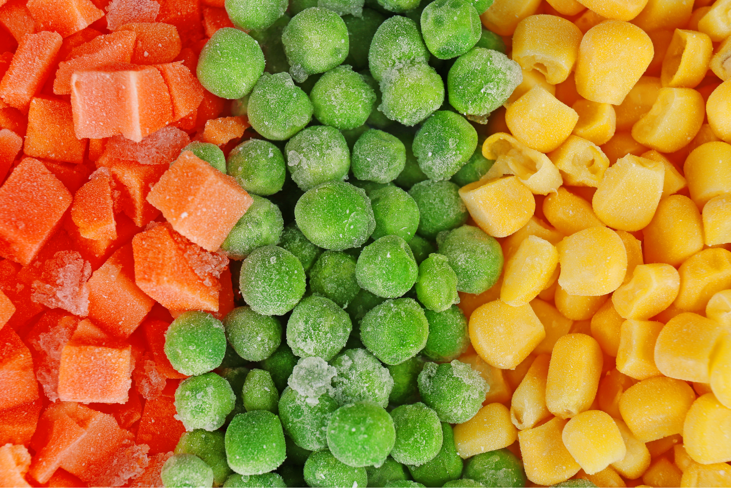 Close-up of frozen mixed vegetables including diced carrots, green peas, and corn kernels.