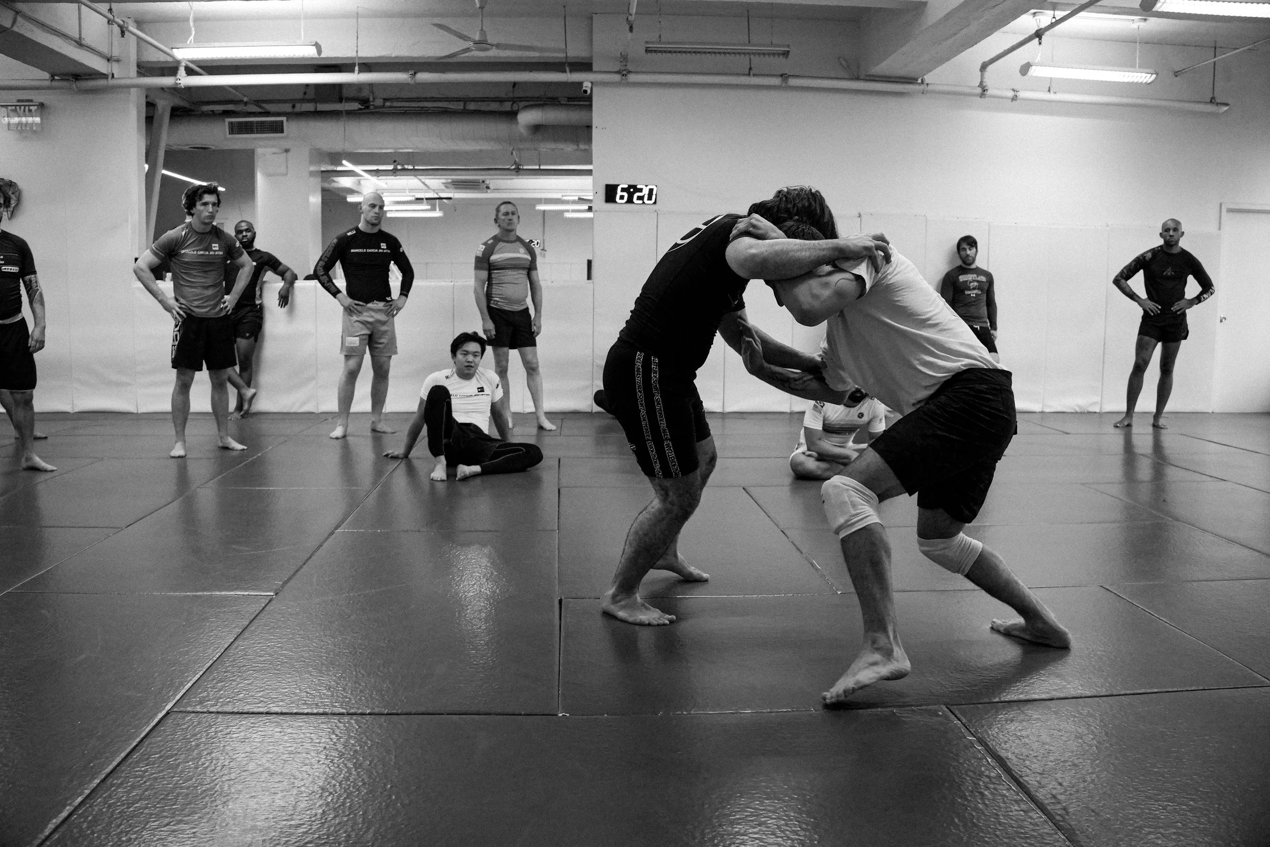 Two individuals grappling and practicing martial arts in a gym, surrounded by onlookers.