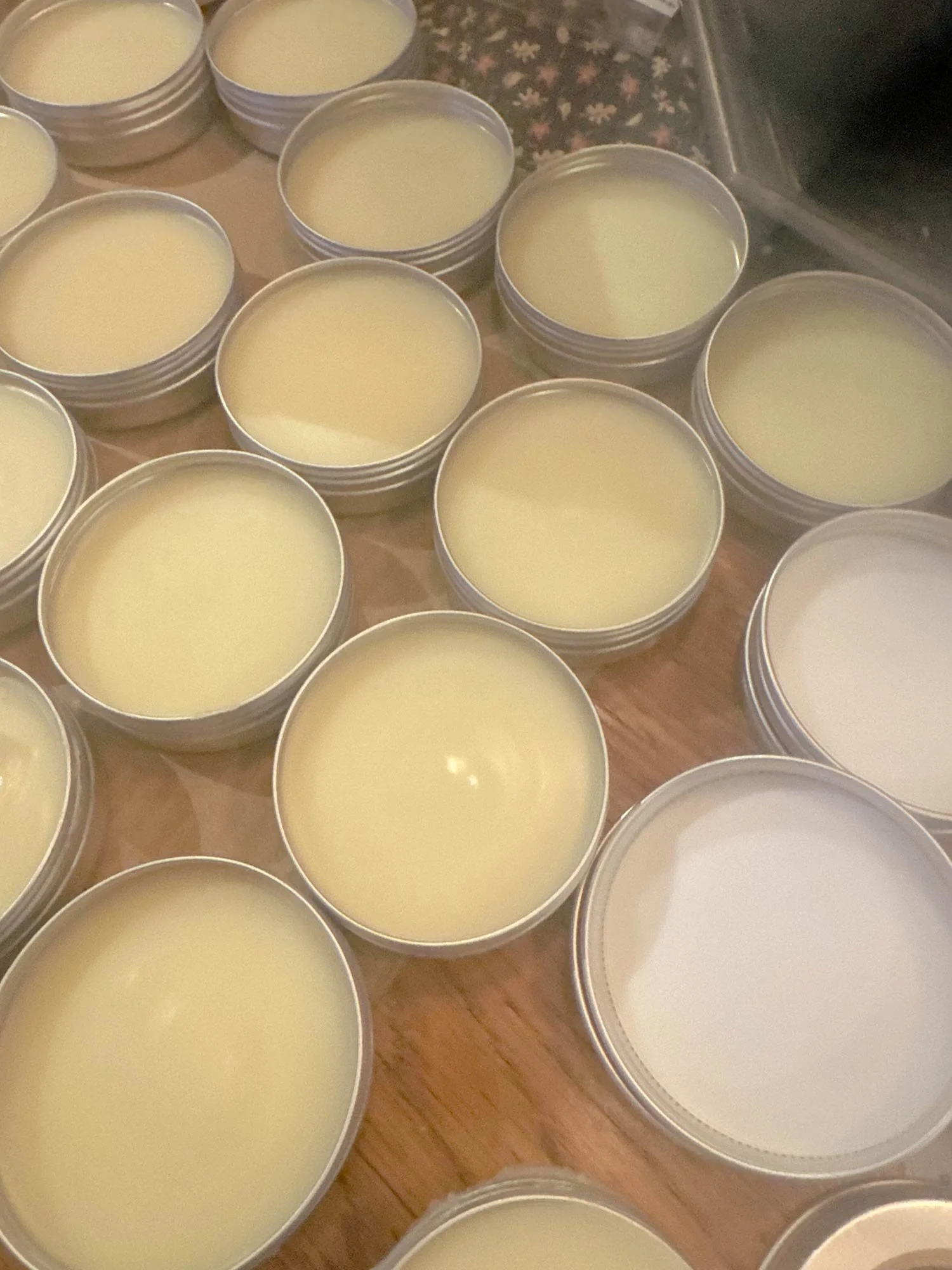 Multiple small tin containers filled with lip balm on a wooden surface.