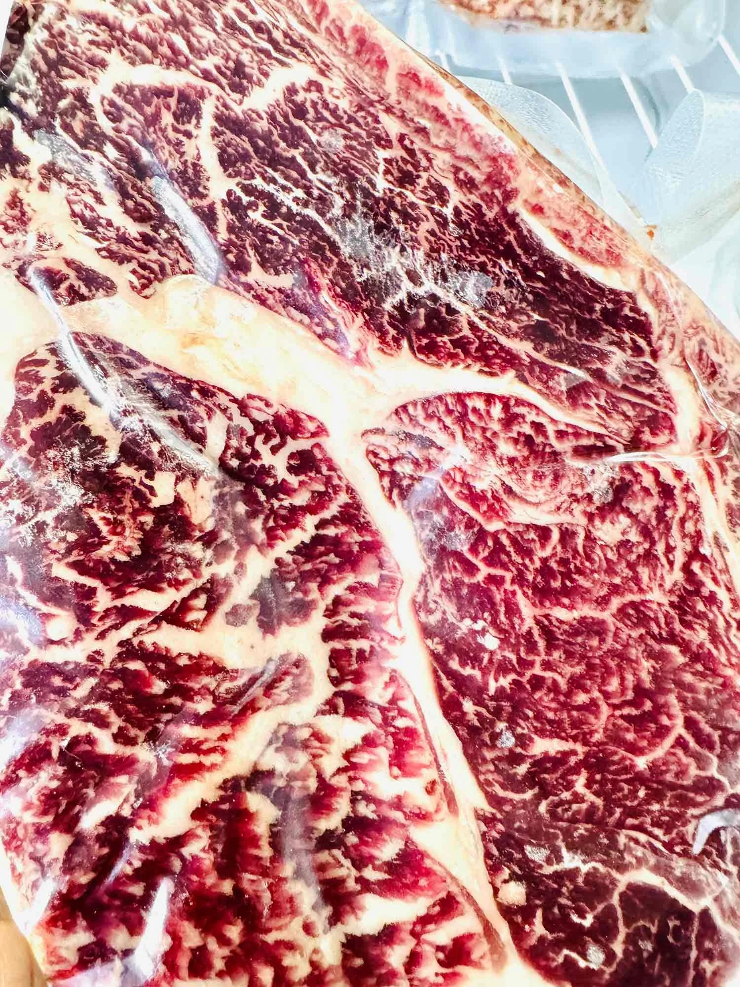 Close-up of raw beef with marbling, sealed in plastic packaging.
