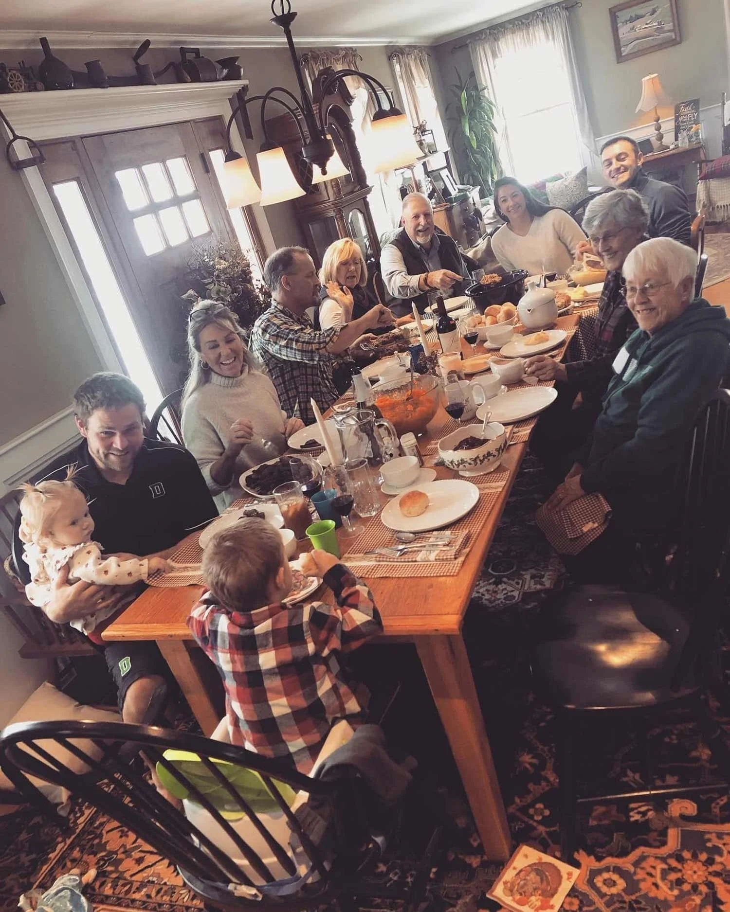 Family gathering around a dining table enjoying a meal in a cozy home with natural light and traditional decor.