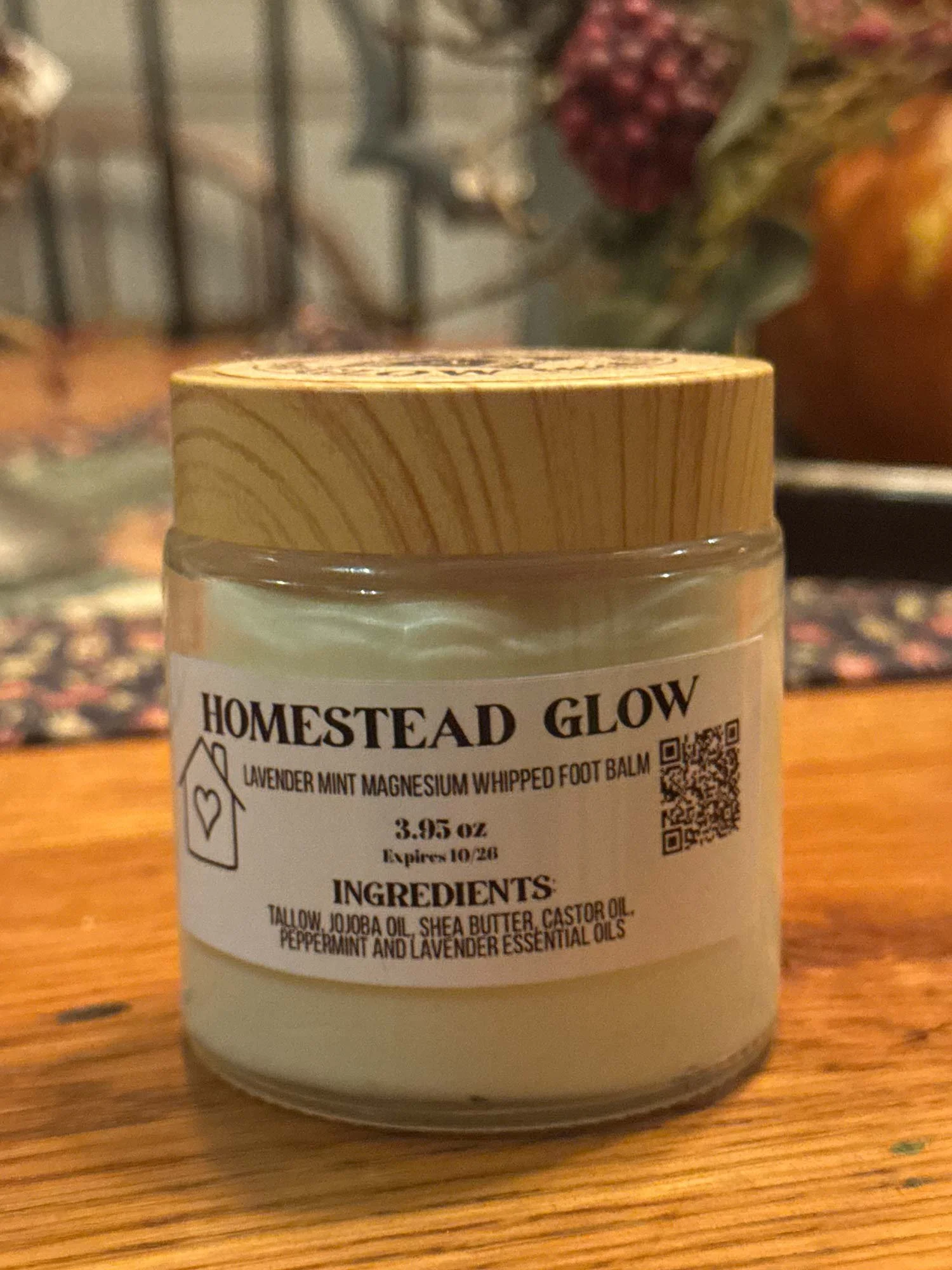 A glass jar of Homestead Glow lavender mint magnesium whipped foot balm with a wooden lid, placed on a wooden surface.