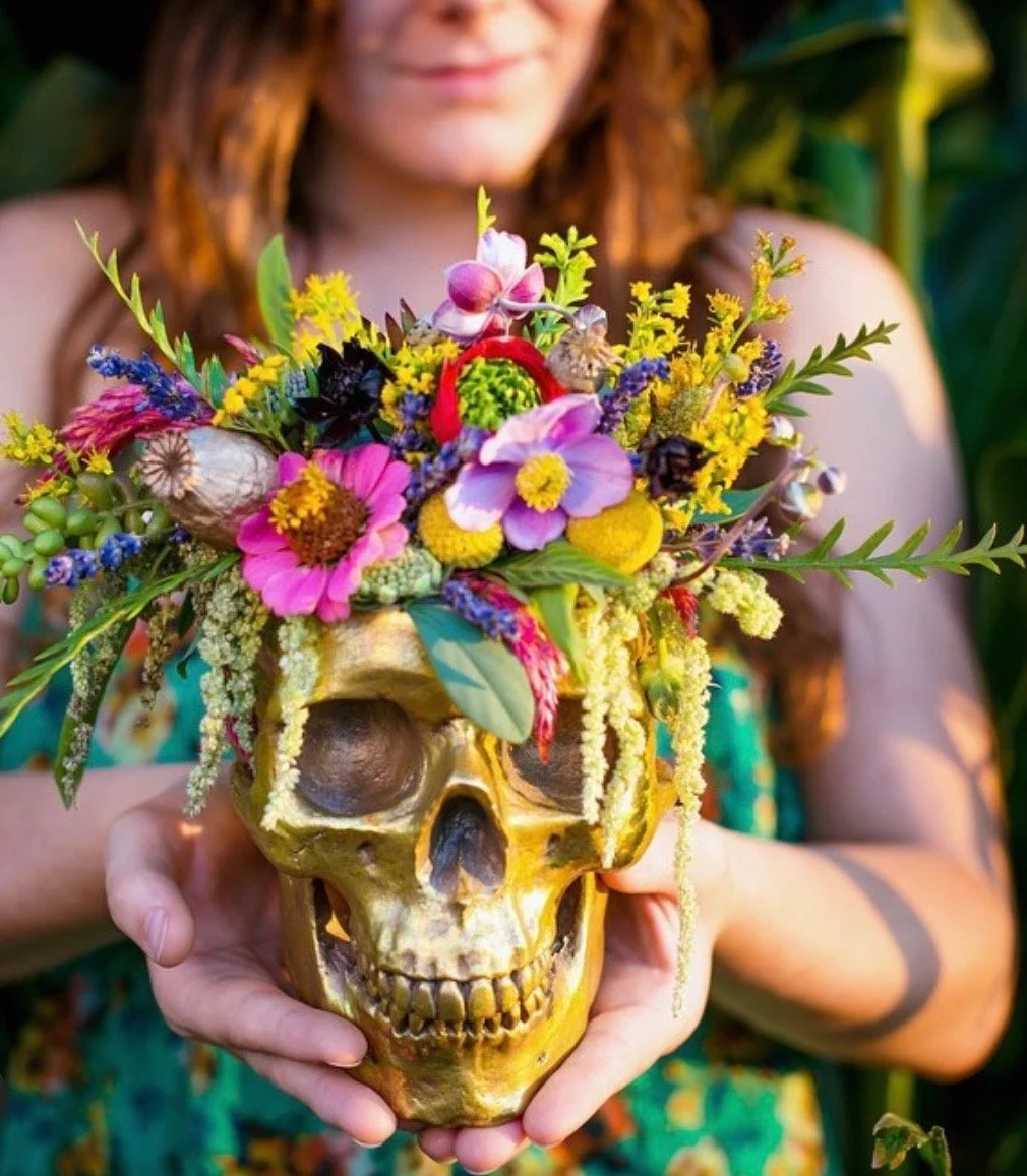 A person holding a skull decorated with colorful flowers and greenery.