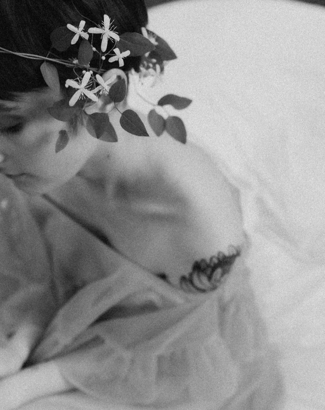 A close-up black-and-white photo of a person's face with a flower and leaves arrangement partially covering their head, with a focus on the lips and nose.