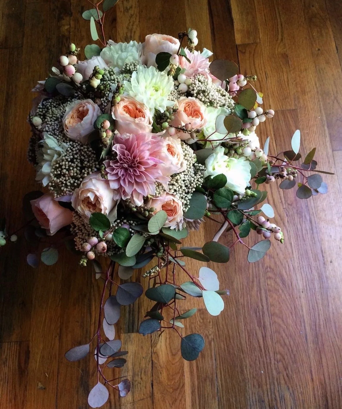 A bouquet of light pink, white, and peach flowers with green leaves and small white berries on a wooden surface.