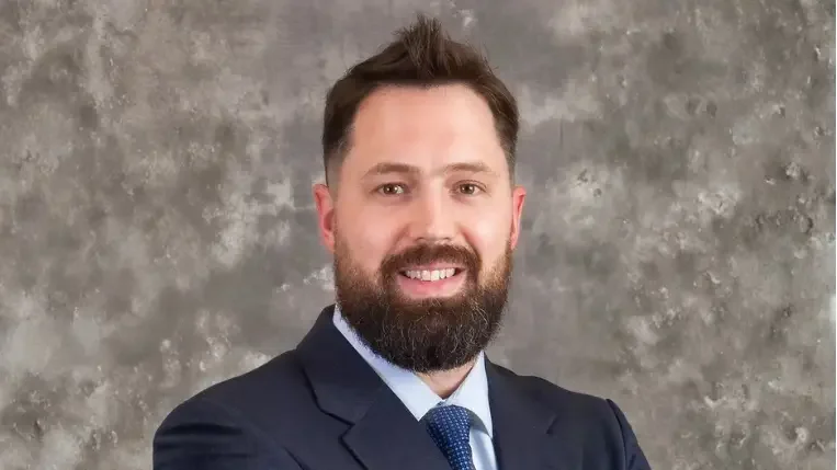 photo of Neil Poulsen MD in a suit and tie smiling with a gray blurry background