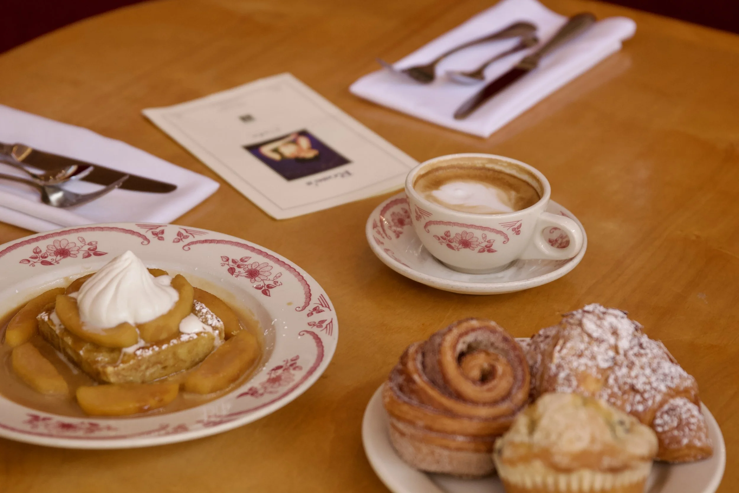 Breakfast pastries and a latte displayed beautifully on matching tableware with a red floral pattern