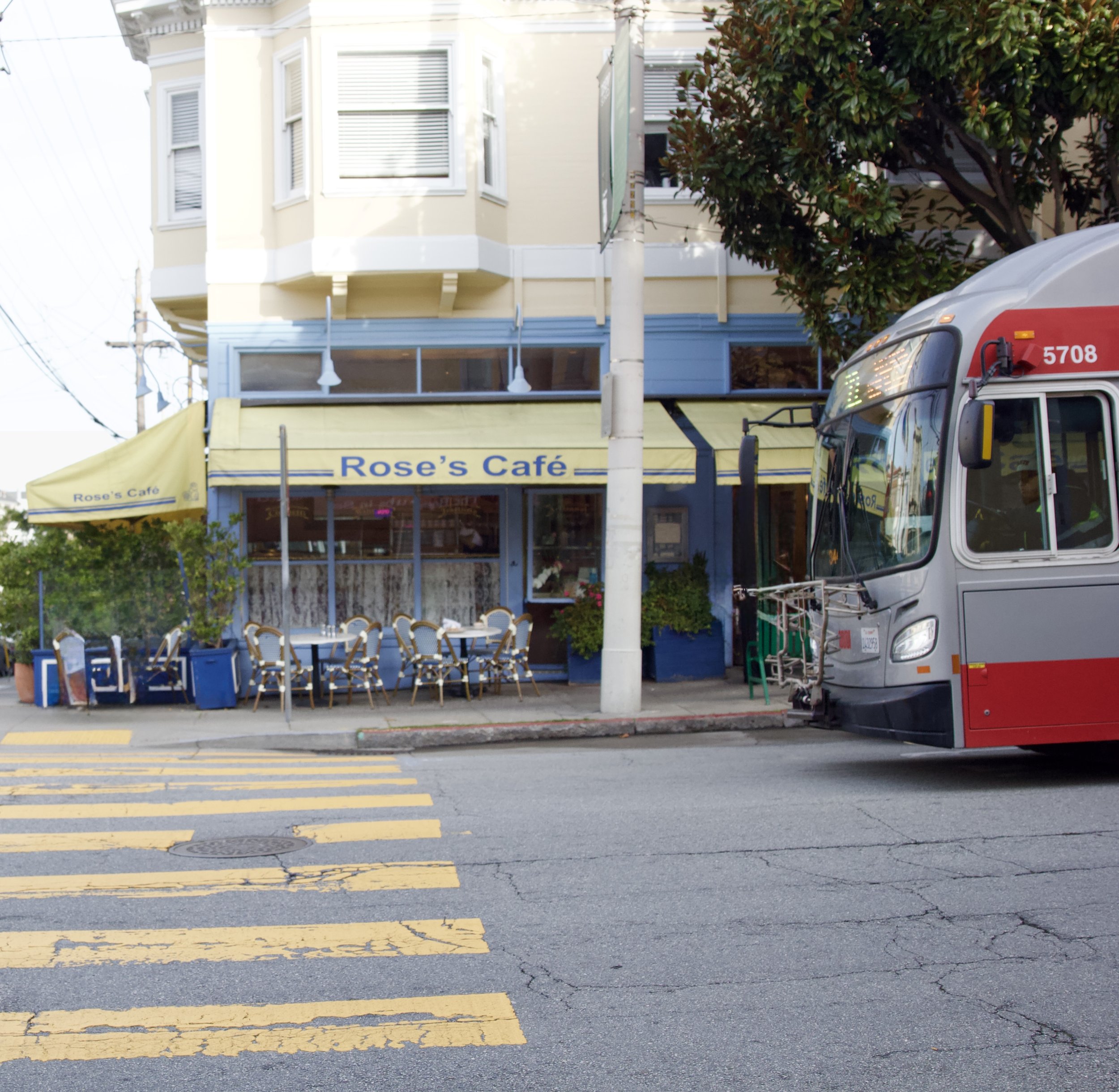 View of Rose's Cafe from across the street showcasing the bistro patio seating, signature yellow awnings and blue exterior paint