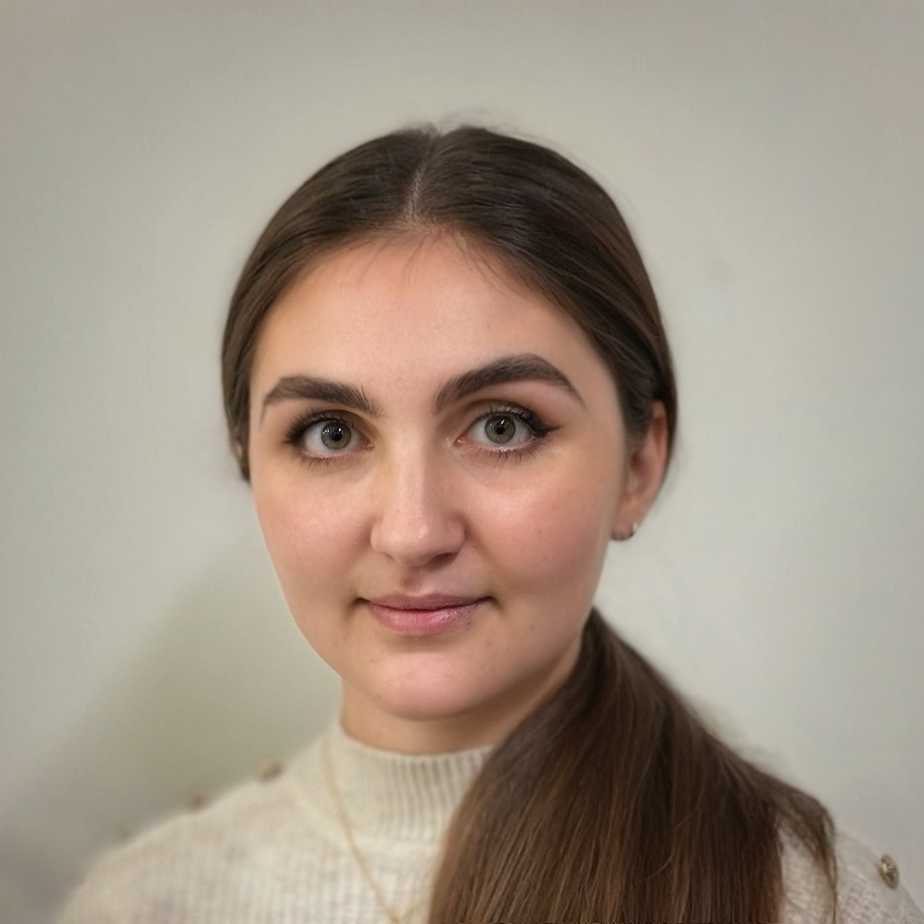Portrait of a young woman with long brown hair, wearing a beige sweater, looking at the camera against a plain light-colored background.