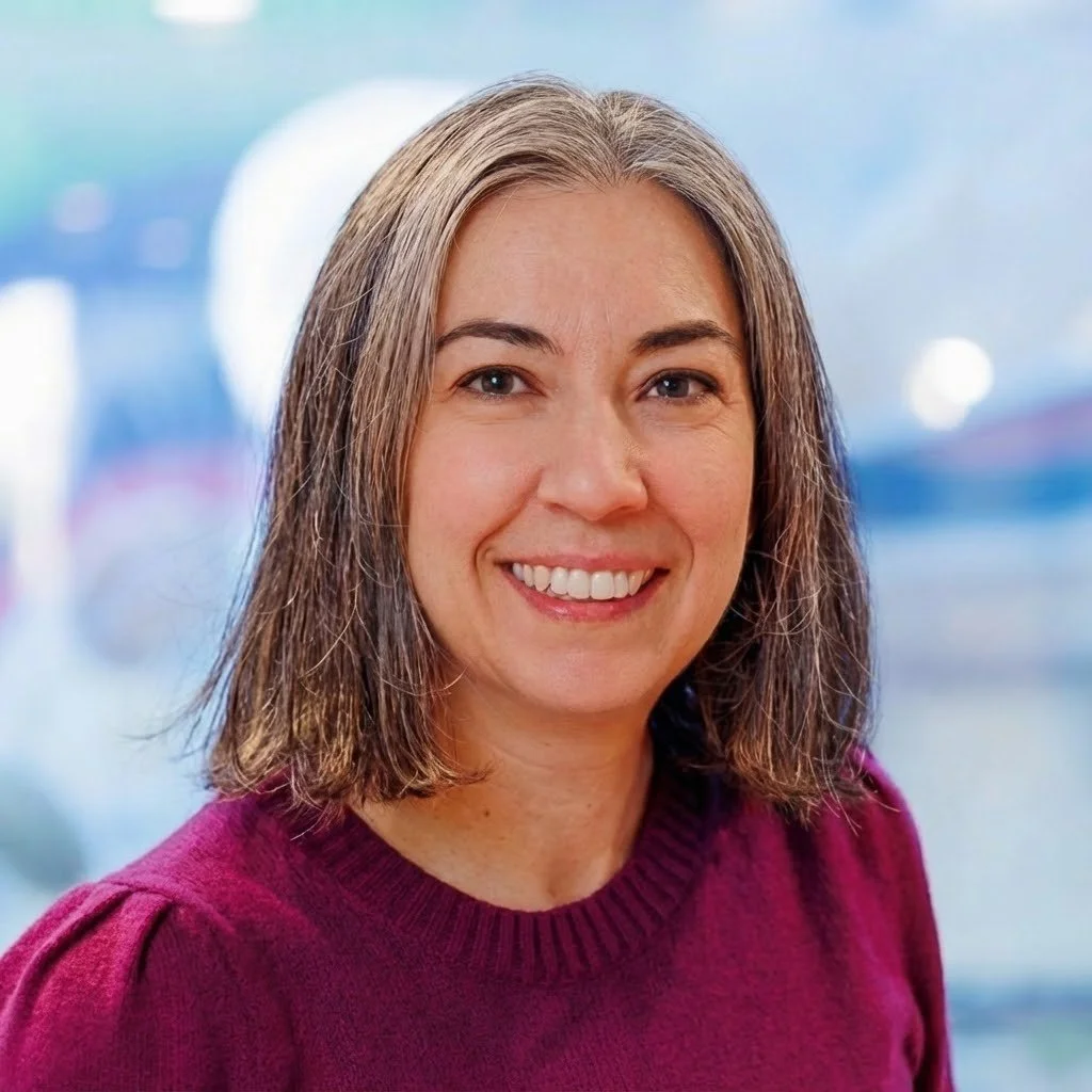Smiling woman with shoulder-length brown hair wearing a maroon sweater, with a blurred background.