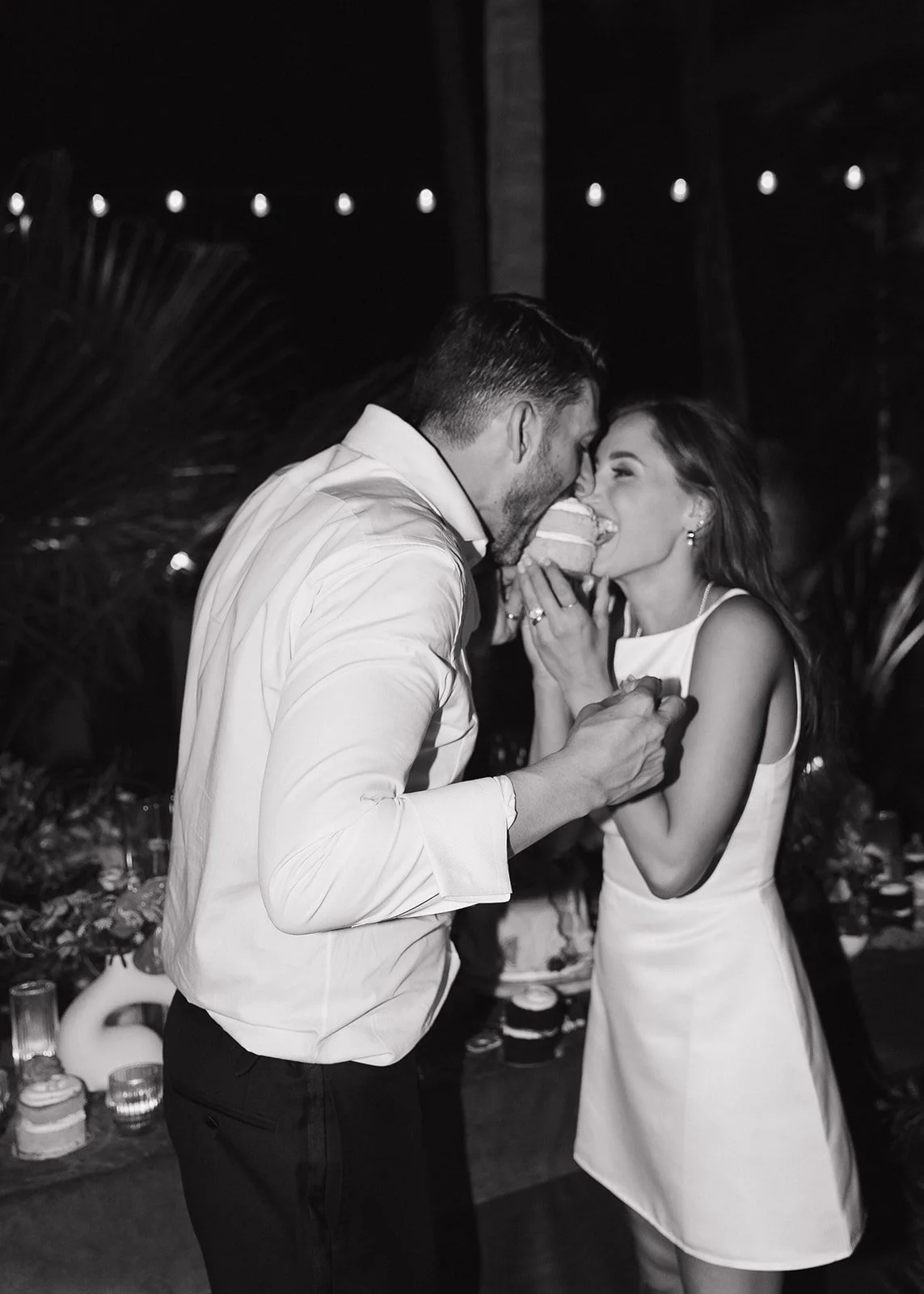 Bride and groom share a bite of cake at this nighttime reception.
