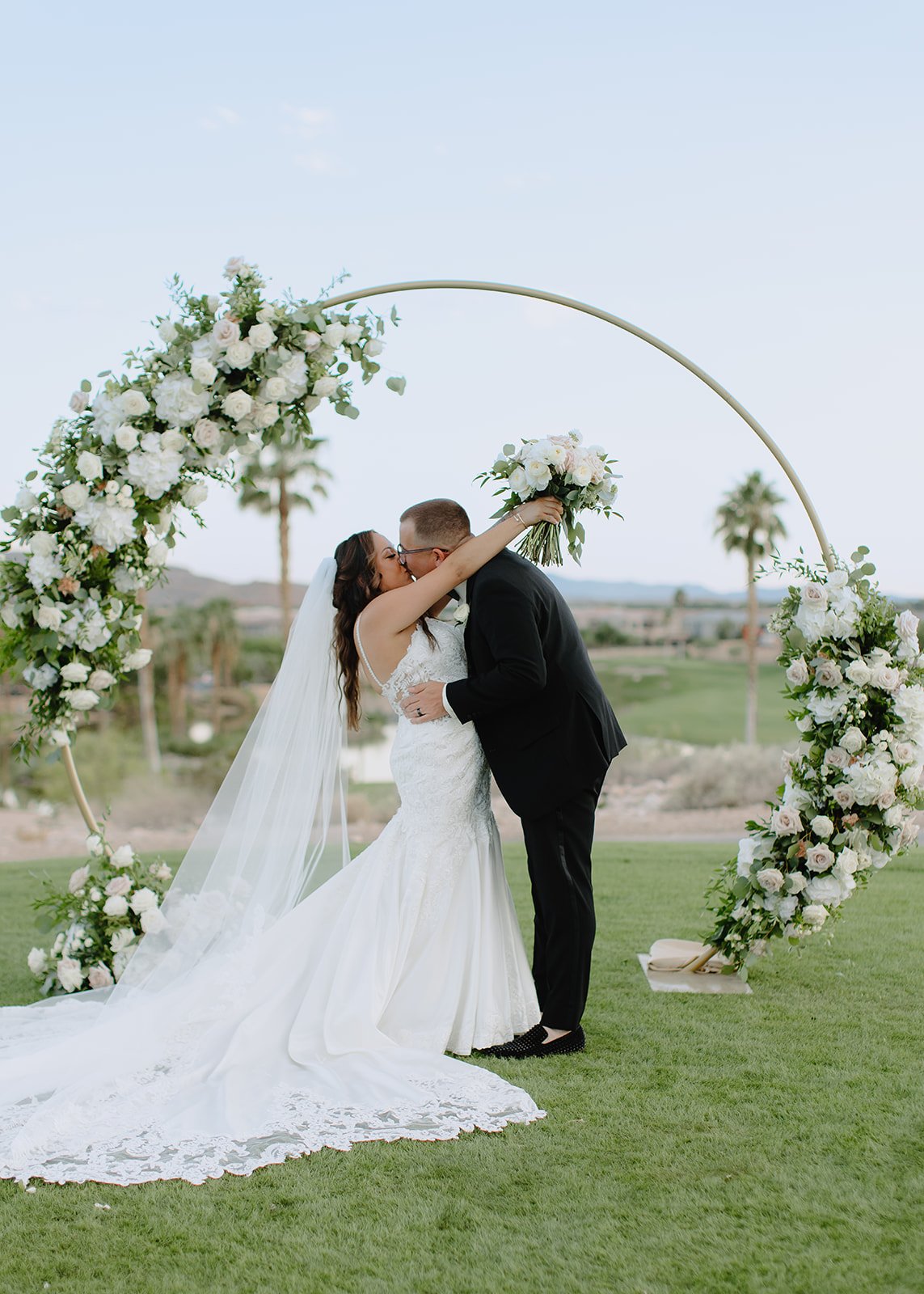 Romantic ceremony moment captured as bride & groom kiss at the floral arch altar.