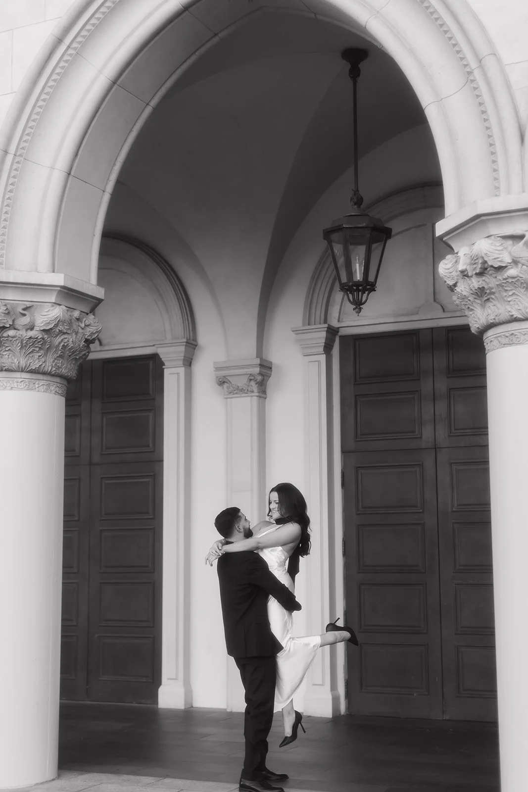 Couple beneath archway as groom lifts bride during engagement portrait.