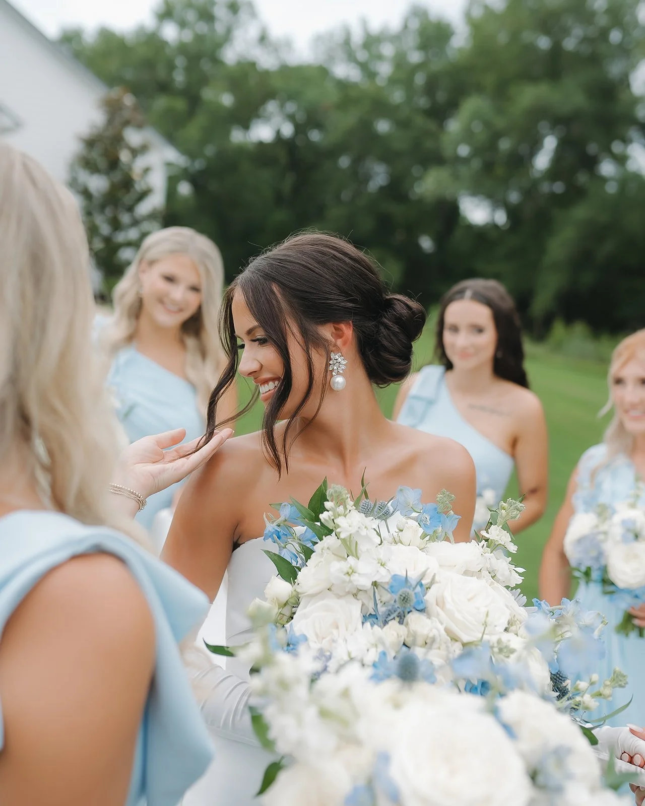 Bride sharing candid moment with bridesmaids during outdoor wedding portrait.