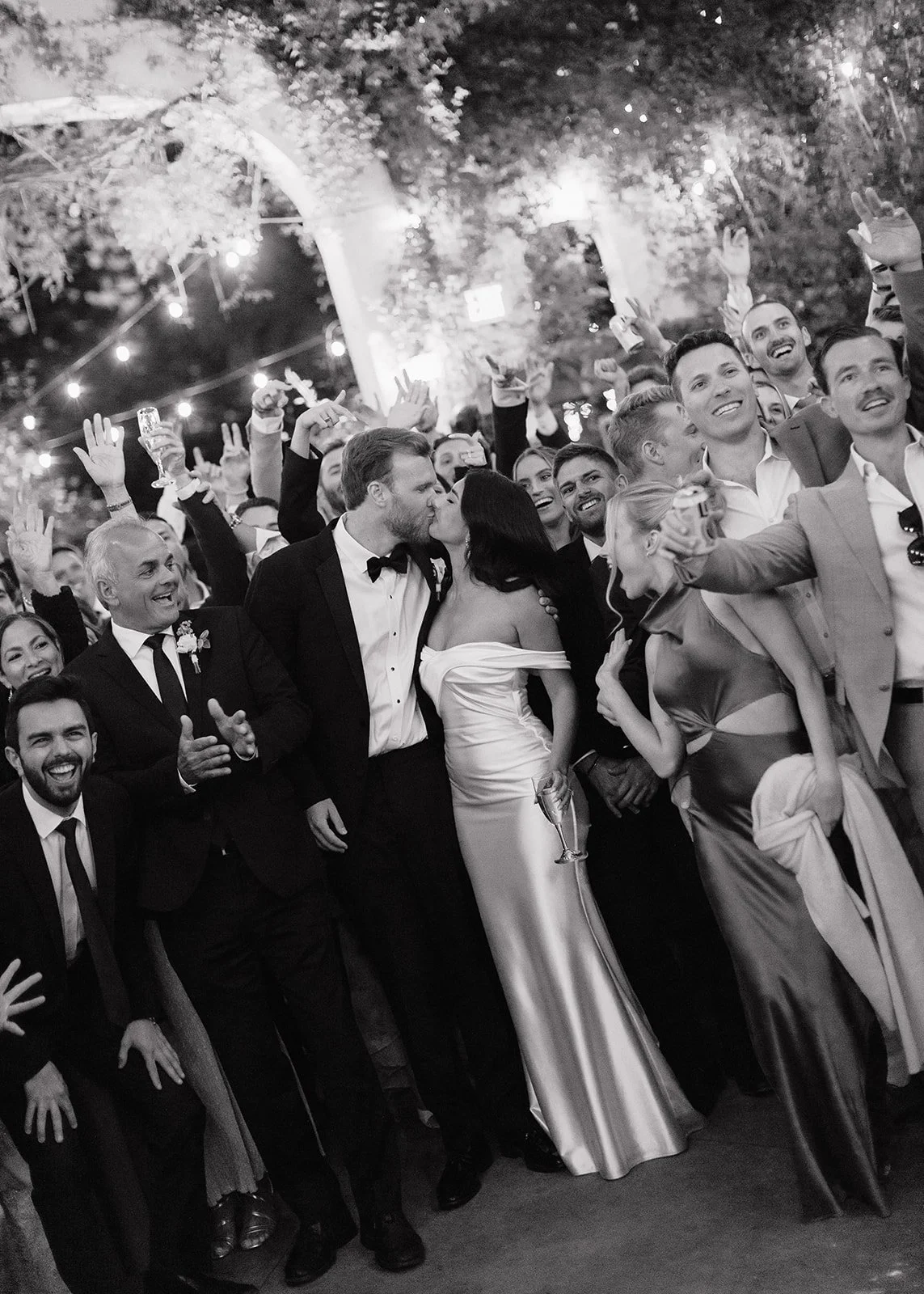 Bride and groom share a kiss in group photo with their guests.