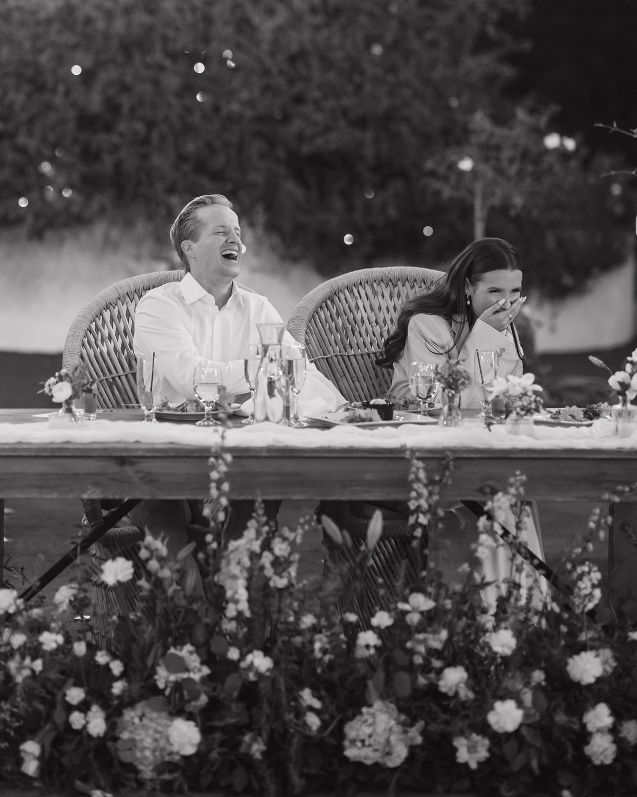 Bride and groom laughing at sweetheart table during speeches.