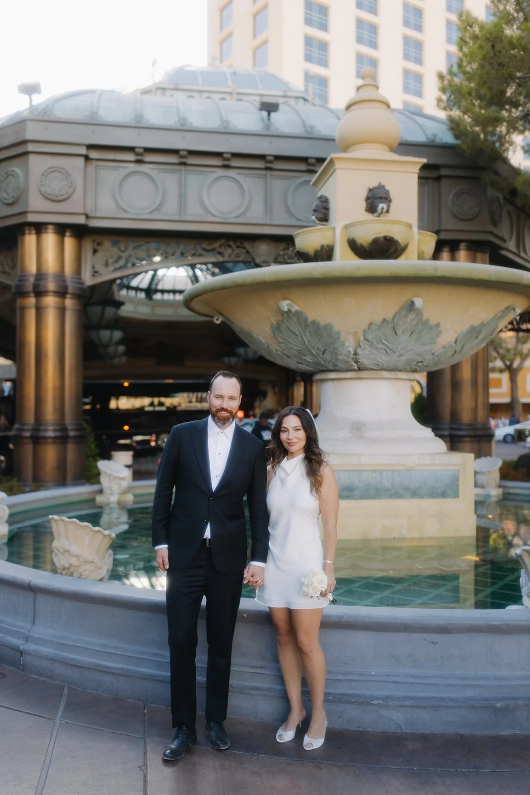 Couple posed beside fountain during elegant engagement portrait.