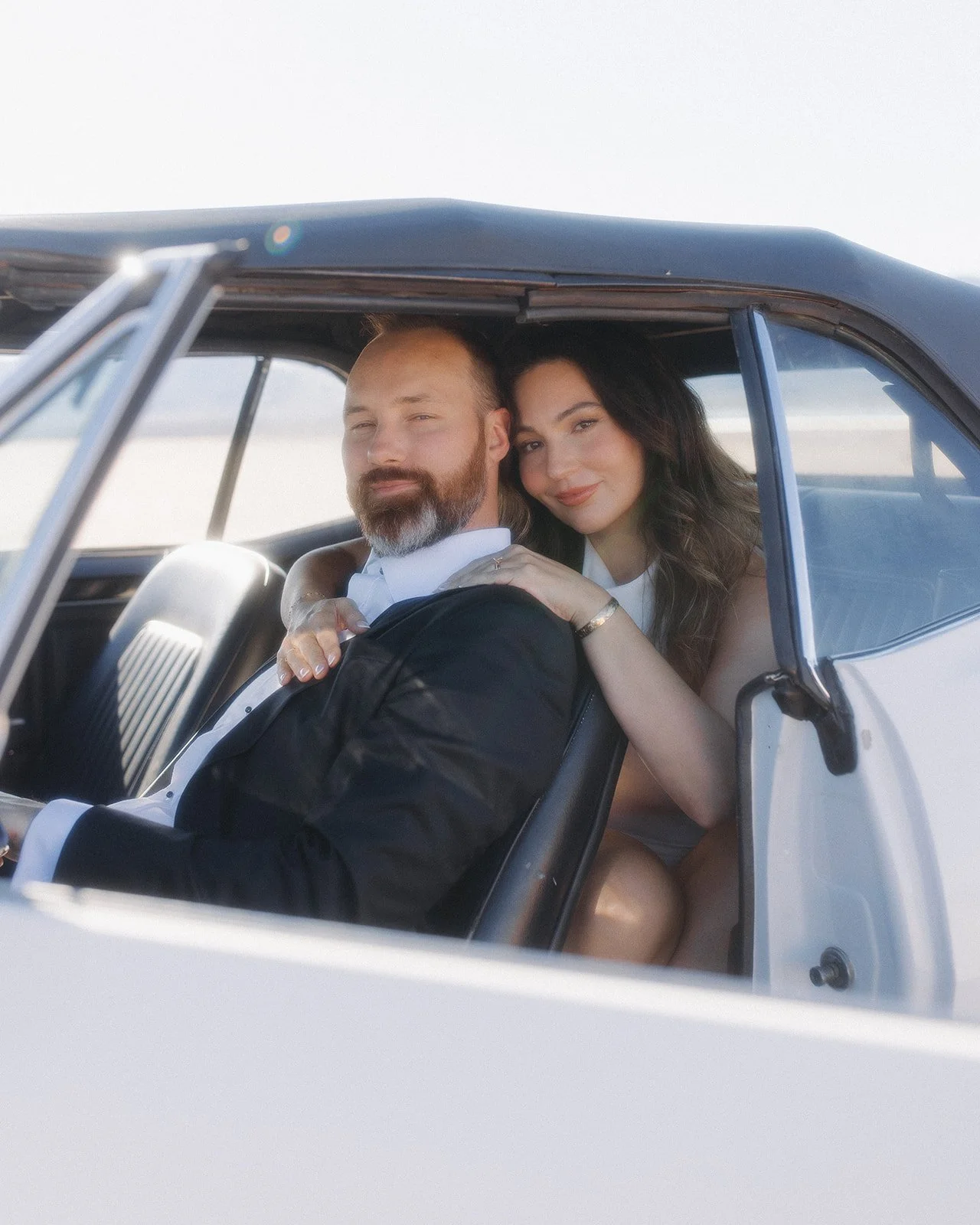 Couple posed with vintage car during styled engagement portrait.