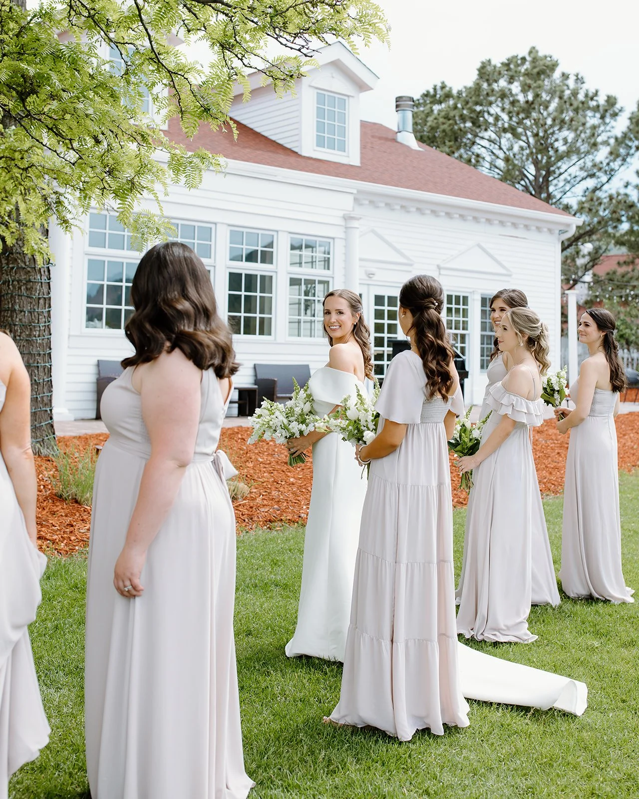 Bride standing outdoors with bridesmaids during wedding portrait.
