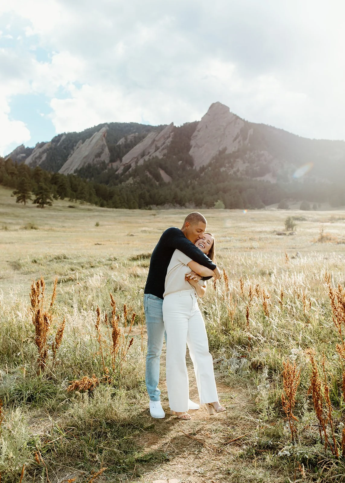 Couple sharing candid embrace in open green space during portrait session.