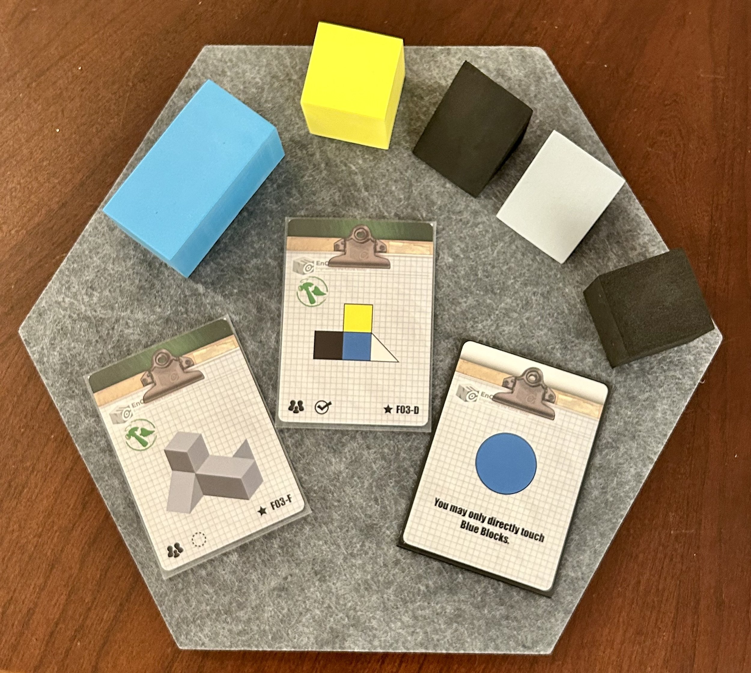 Three cards with geometric shapes and four colored blocks on a gray surface, with additional black, white, blue, and yellow blocks around.