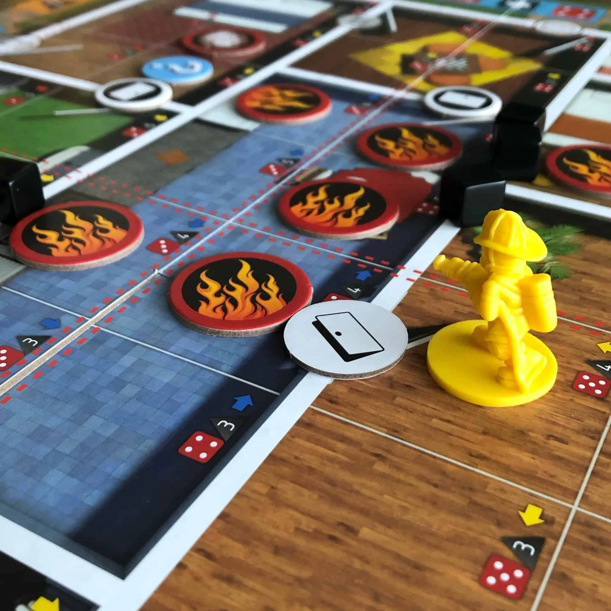 Close-up of a board game with a yellow firefighter pawn, fire icons as game pieces, and a white icon representing a tablet or phone on the game board.