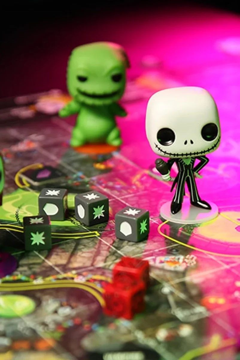 Board game with colorful dice and figurines, including a white skeleton figurine and a green monster figurine, on a neon pink-lit surface.