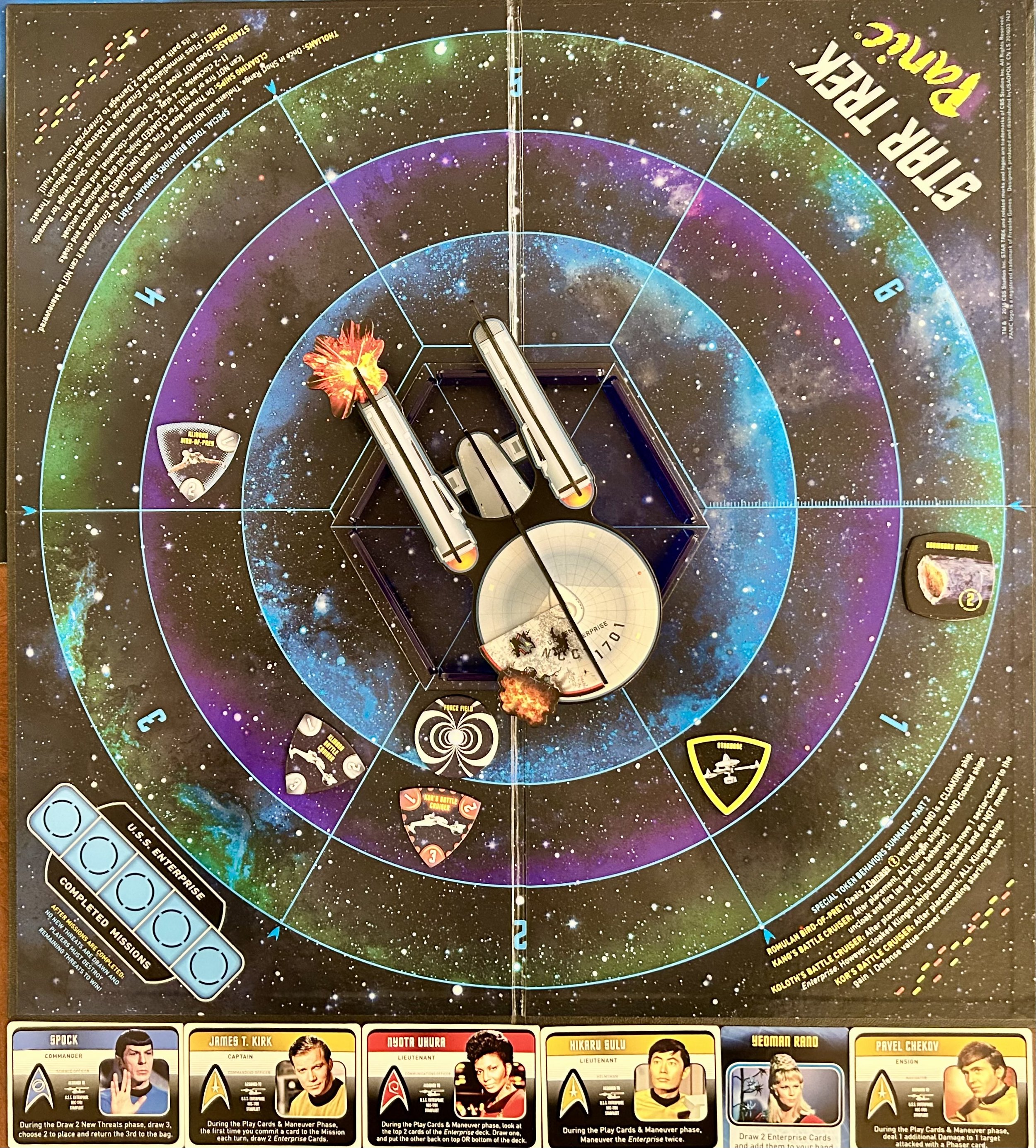 A space-themed game board for Star Trek Attack Wing, with a galaxy background and multiple starship tokens positioned on the board, sides featuring character images from Star Trek, and various game elements such as attack rings and damage tokens.