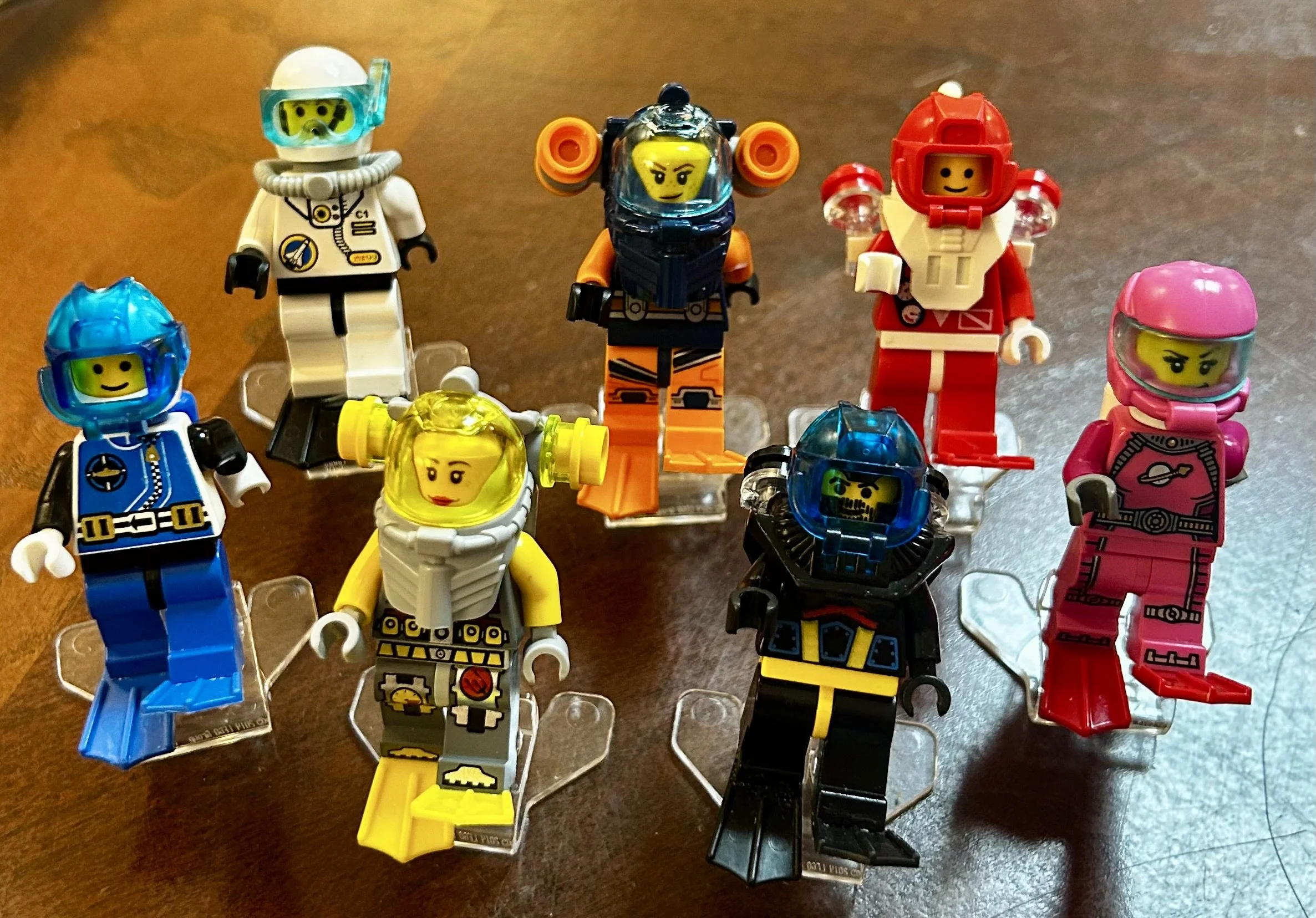 A collection of LEGO mini-figures with space-themed outfits and helmets, displayed on a wooden surface.