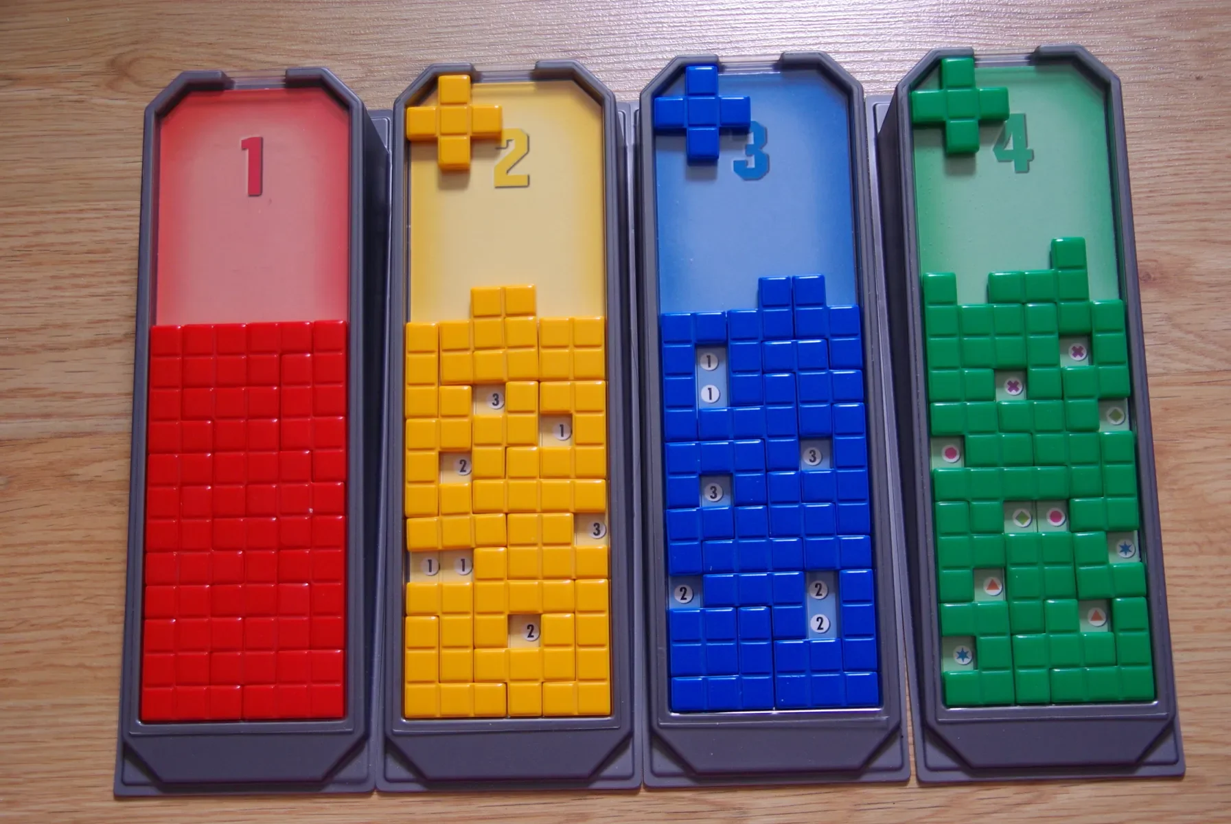Image of four Tetris-style puzzle trays with different colored blocks and numbers on a wooden surface.