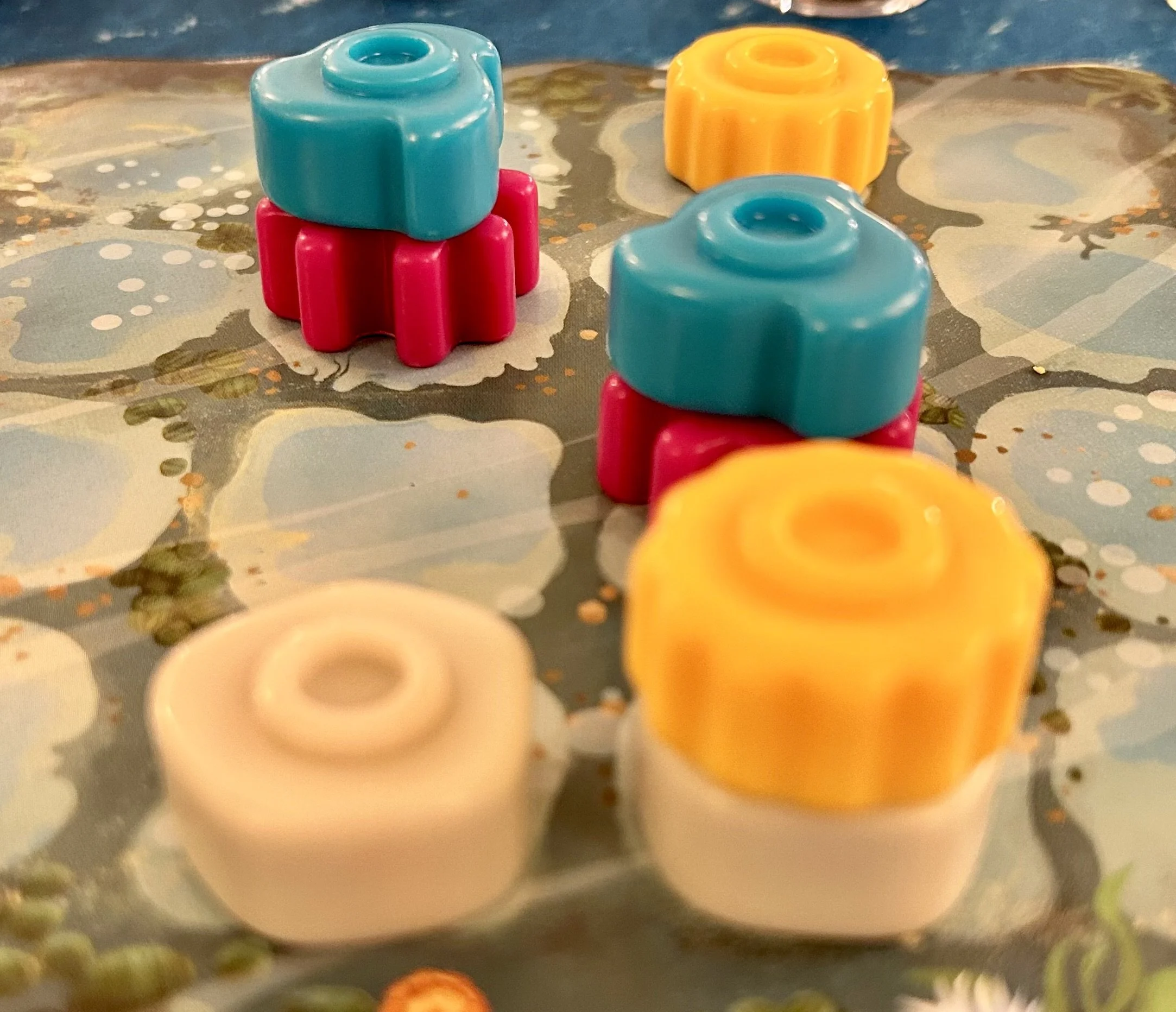 Colorful plastic game pieces in pink, blue, white, and yellow on a patterned surface.