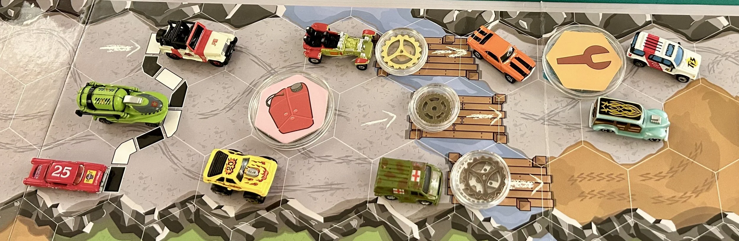 Toy race cars on a board game track with a river and bridge, some with flames designs, and various game pieces including gears and hexagonal tokens.