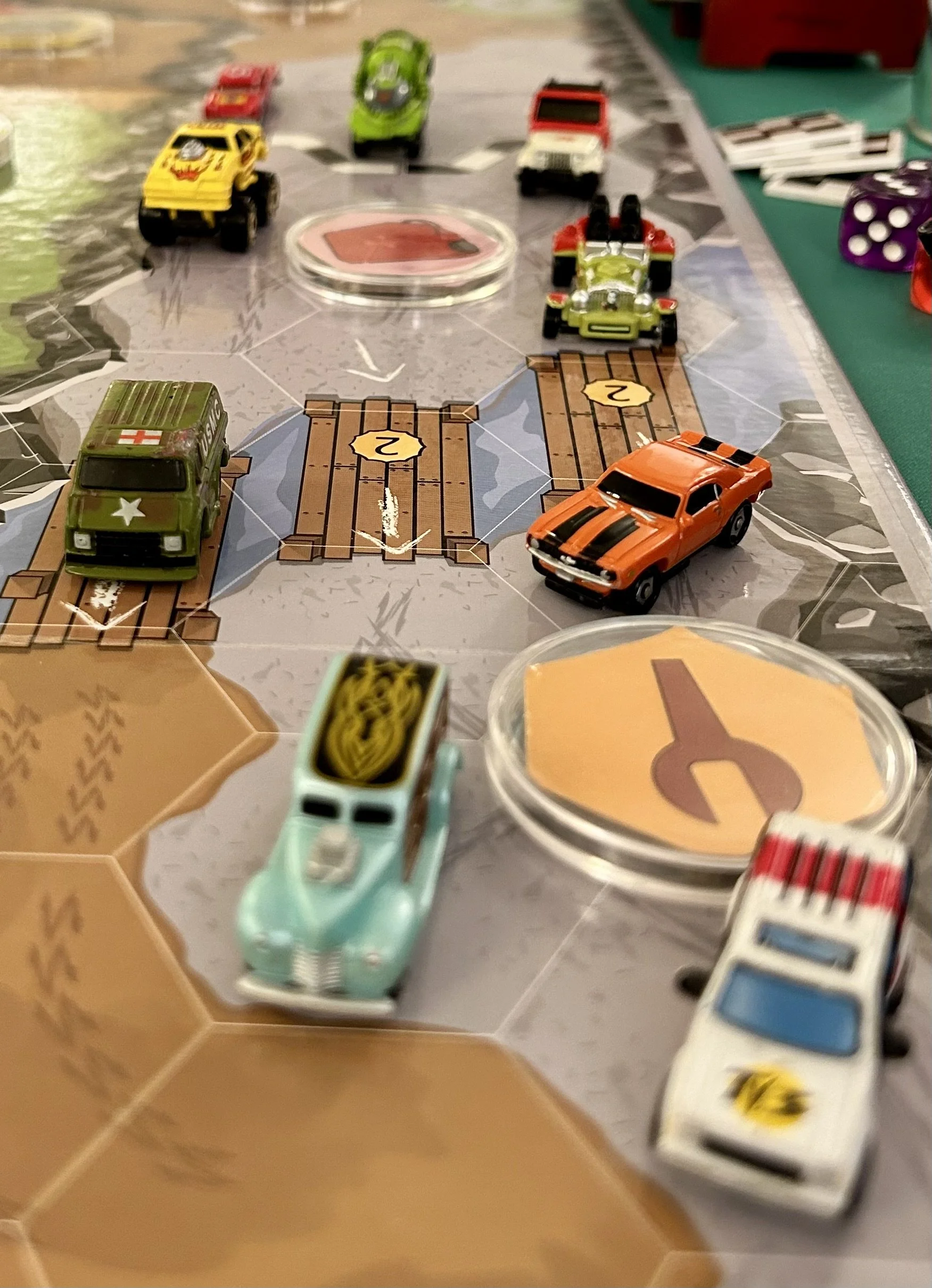 Close-up of a board game with small toy cars and dice on a hexagonal-tile game board.