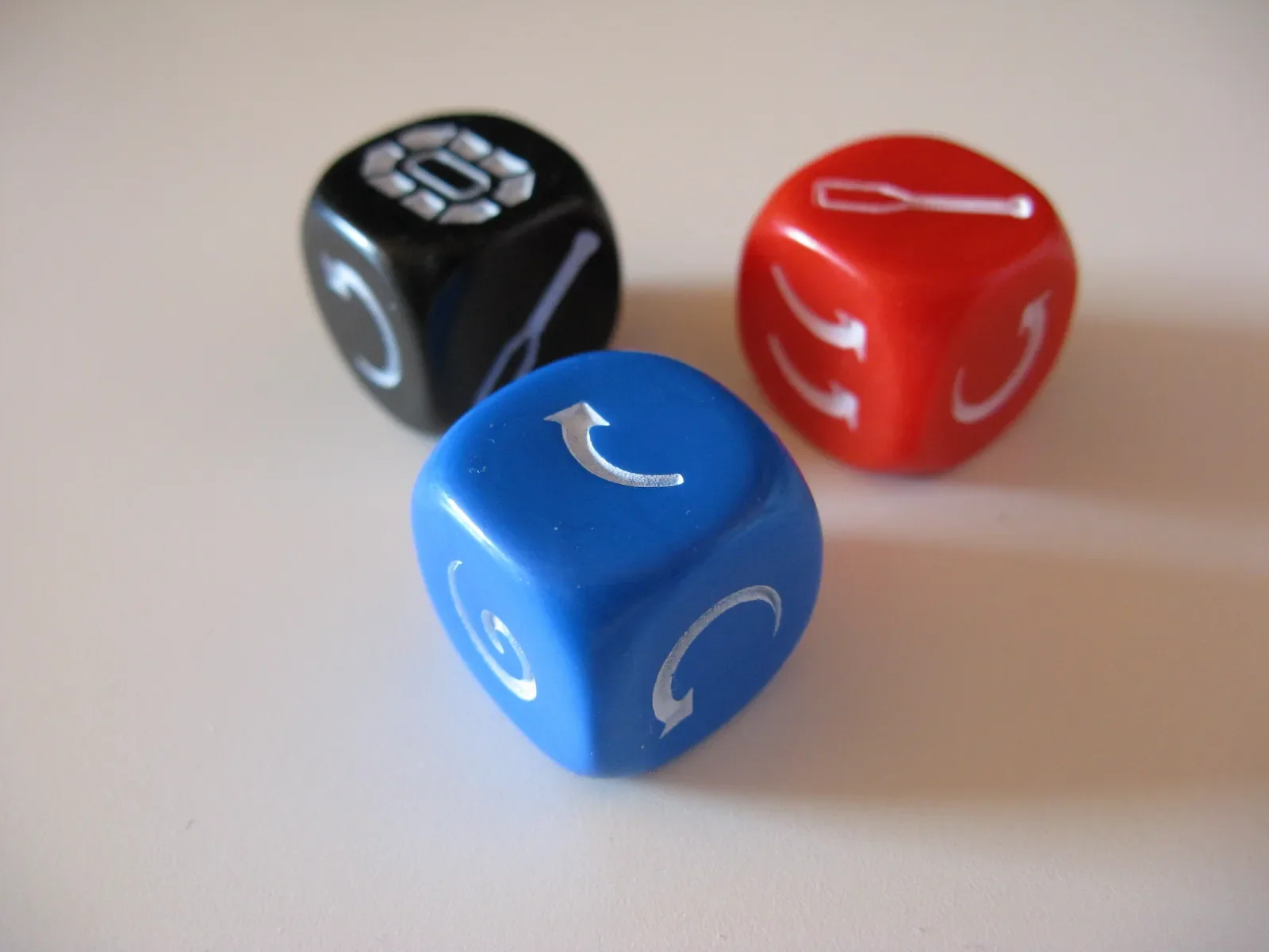 Three colorful gaming dice on a white surface, one blue, one red, and one black, each with white symbols.