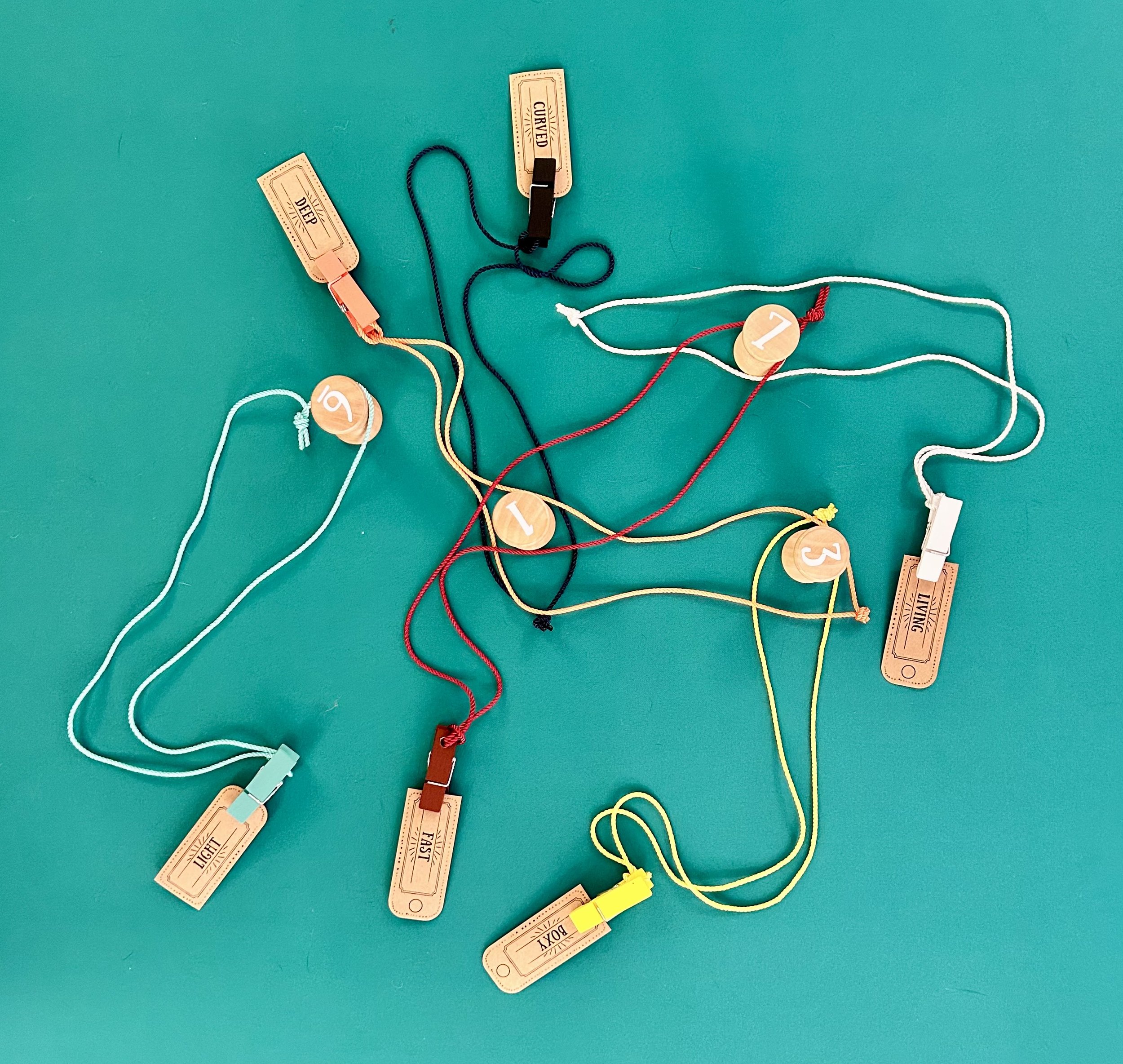 Multiple colorful strings with tags numbered 1 to 6, indicating different attributes like 'Deep', 'Curved', 'Light', 'Fast', 'Living', and 'Doxy', arranged on a teal surface.