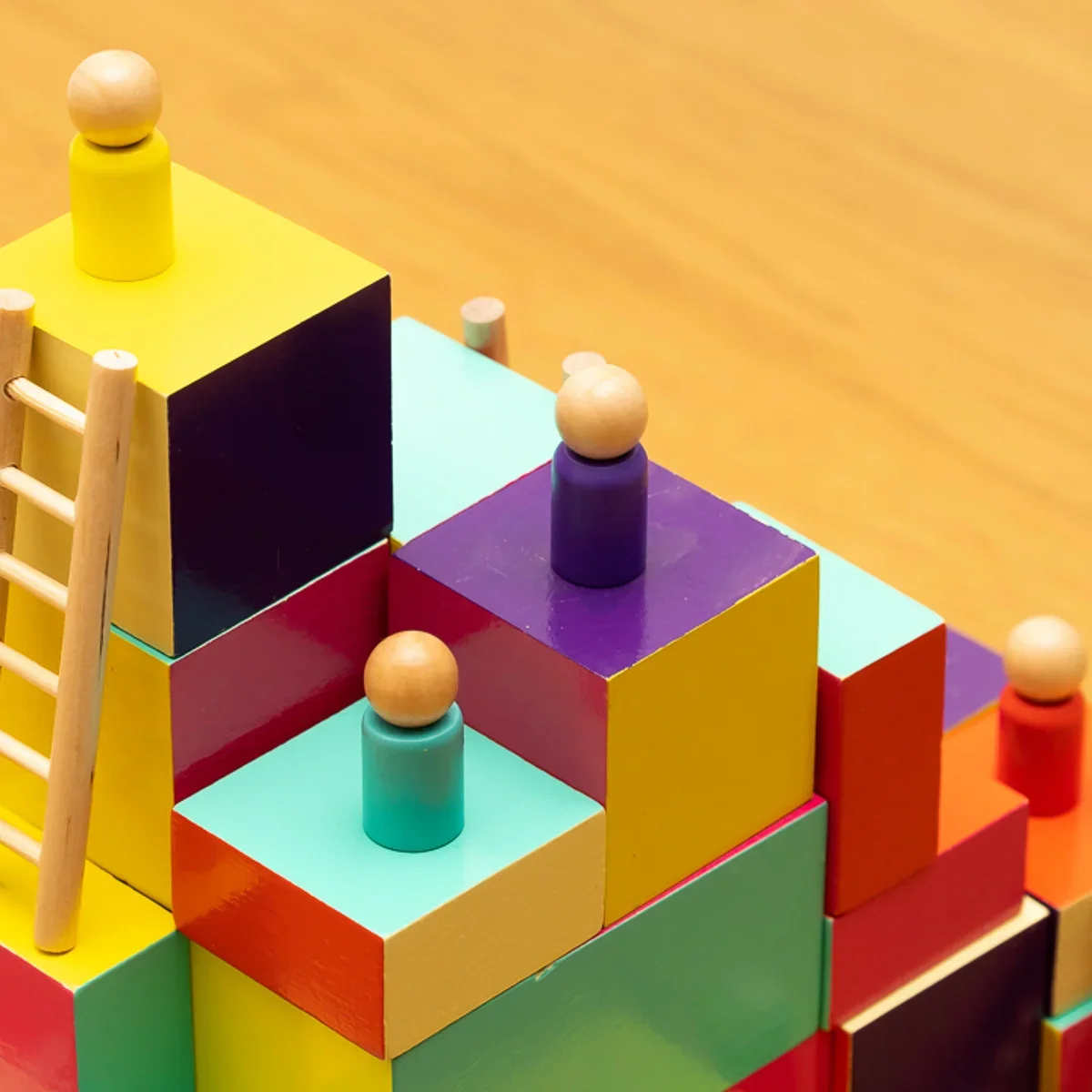 Colorful geometric wooden blocks stacked in a pyramid shape with small wooden balls on top of some blocks, on a wooden surface.