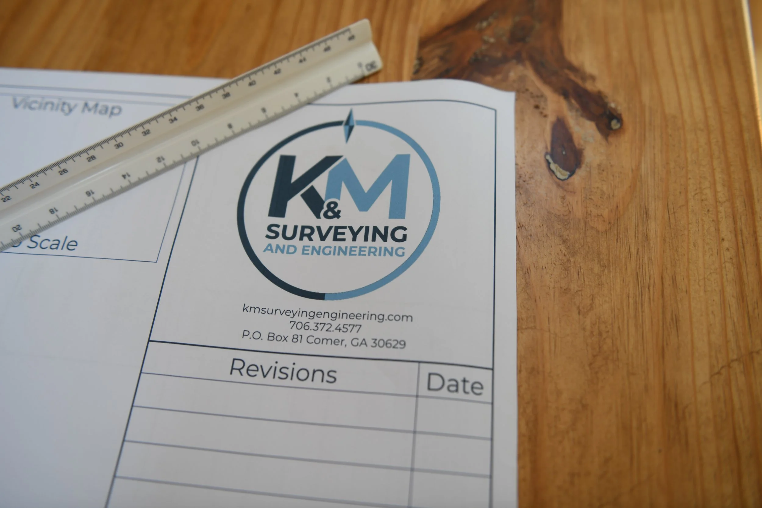 Close-up of a survey or engineering form with a logo that reads "K&M Surveying and Engineering" and a 30-centimeter ruler placed diagonally across the paper on a wooden surface.