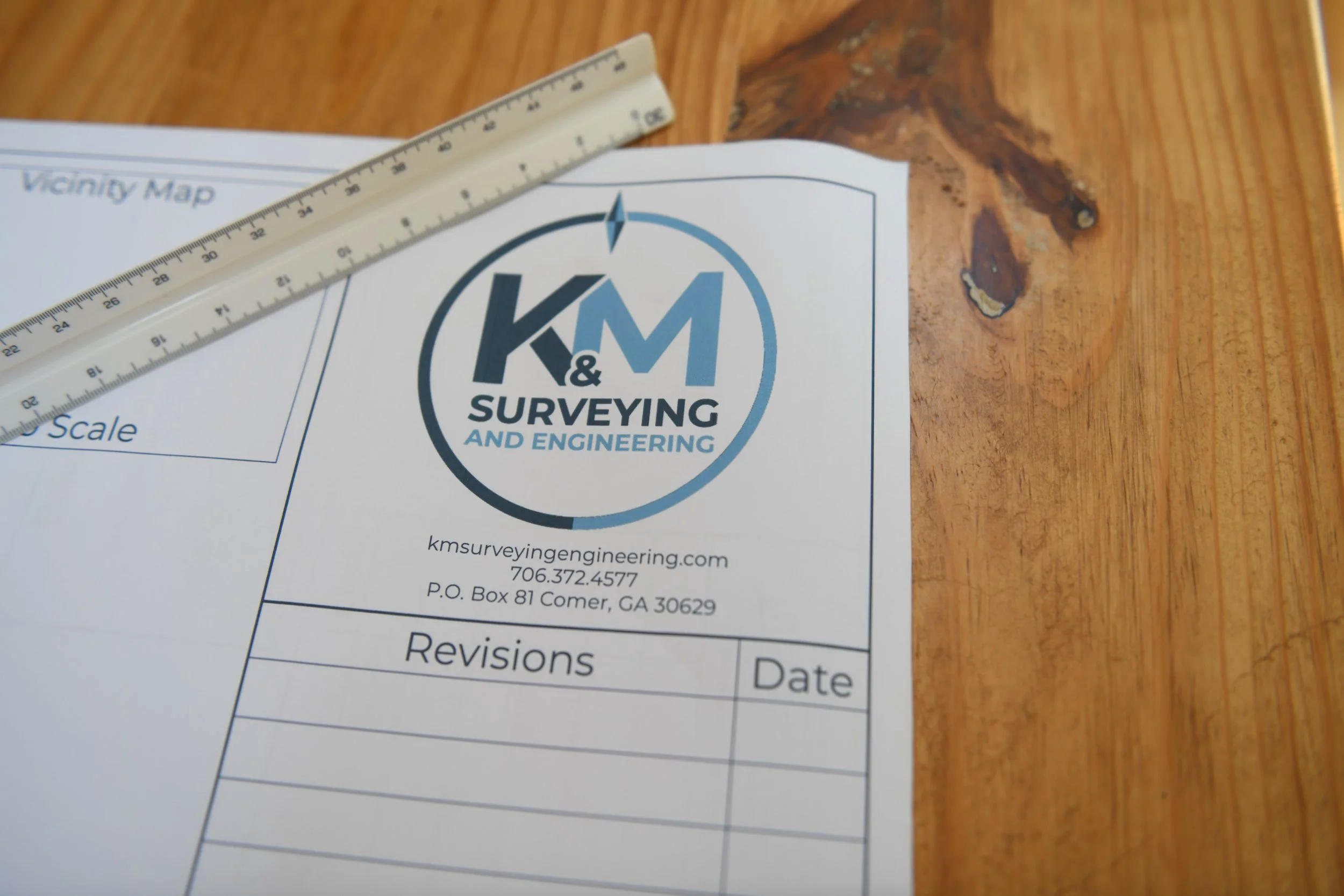 A survey and engineering document featuring a K&M logo and a ruler placed diagonally on a wooden surface.
