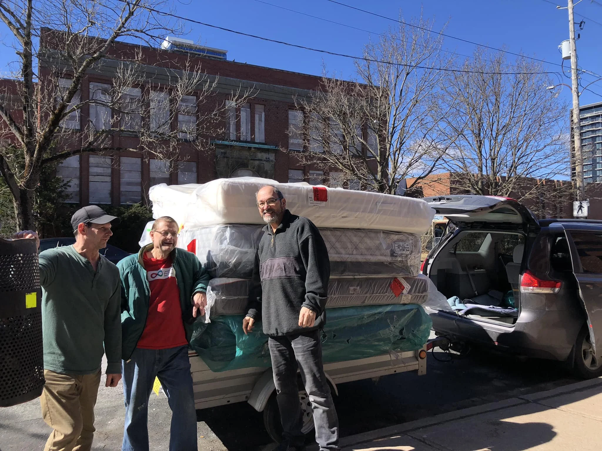 Three volunteers rest as they unload mattresses to be delivered to Nova Horizon clients. tand with truck and stack of mattresses they are delivering.