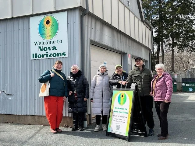 Volunteers stand outside the Nova Horizons building with a new standing around a new Welcome sign.