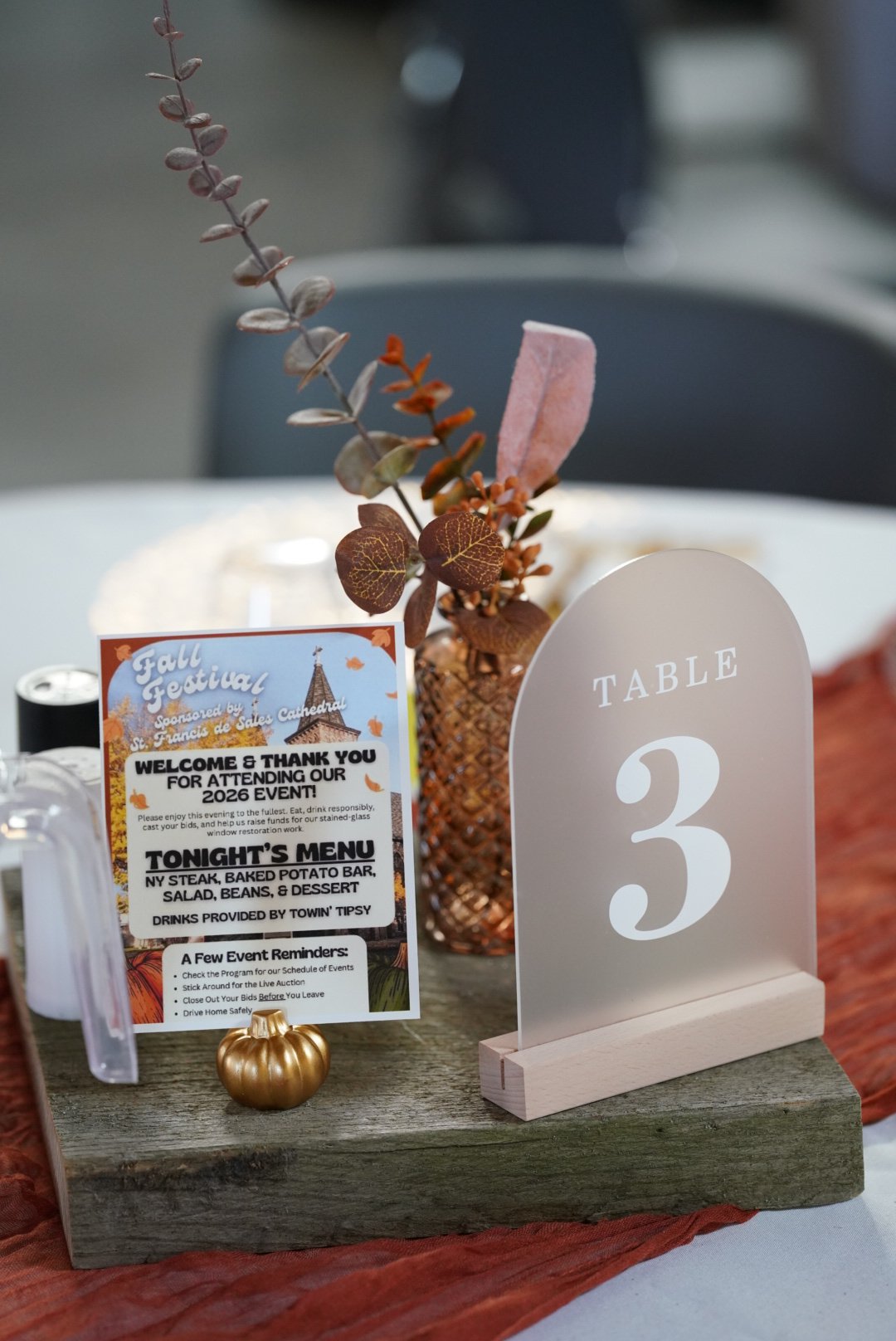 Table number with wood block center piece, amber vase with fake flowers, and gold pumpkin placeholder