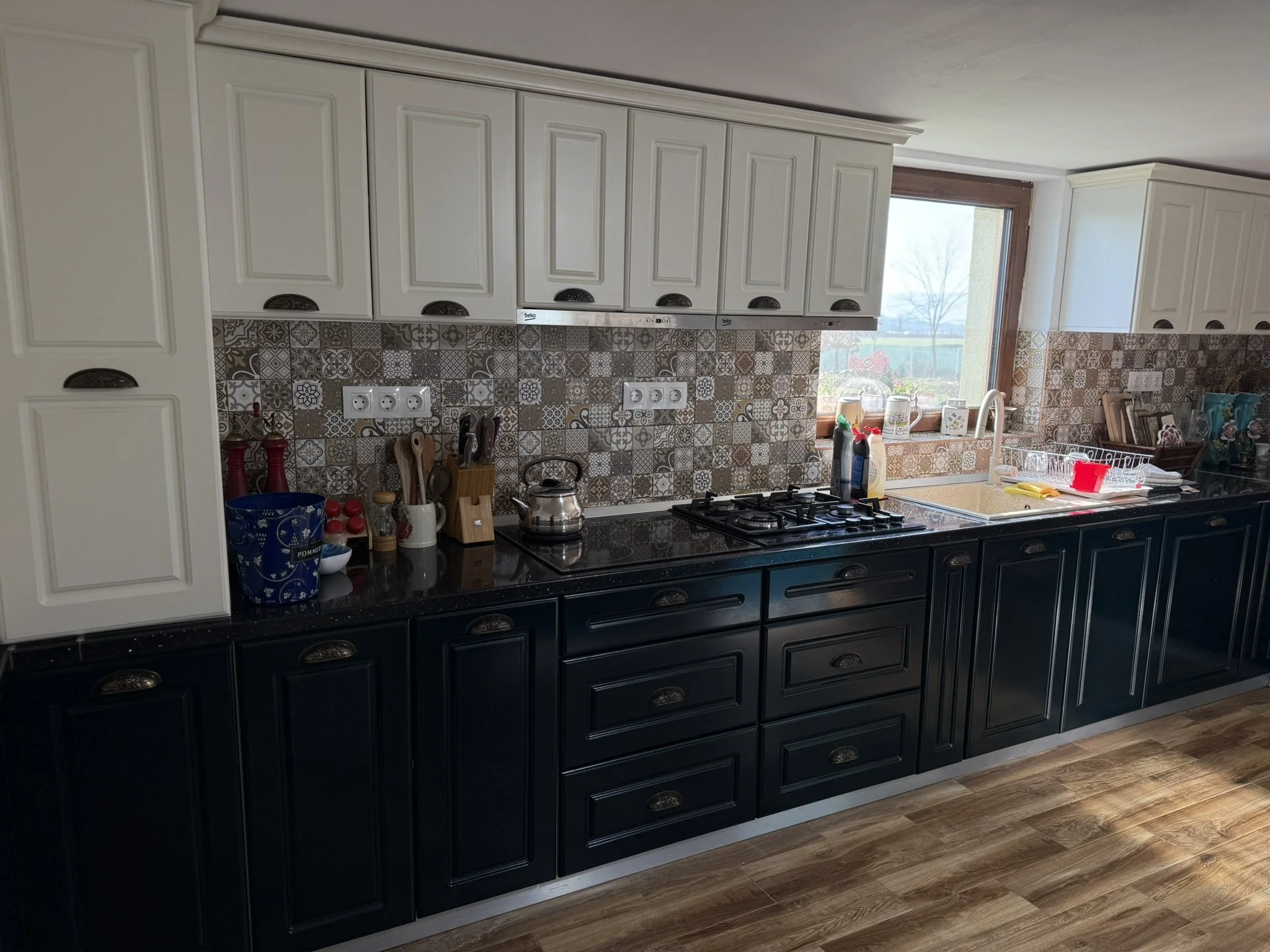 Kitchen with black lower cabinets, white upper cabinets, a patterned tile backsplash, and a window above the sink.