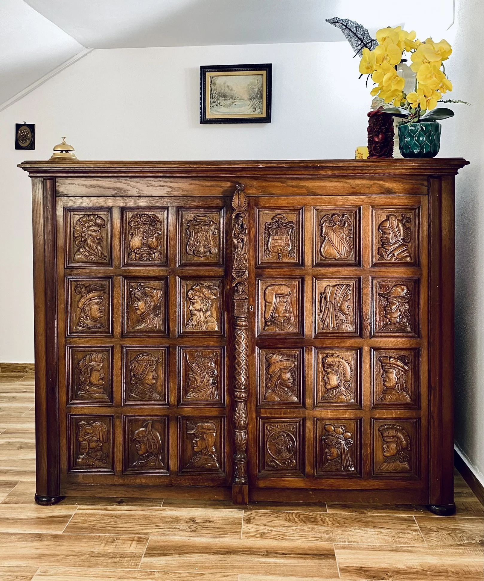 Decorative wooden cabinet with carved portraits of historical figures, topped with a vase of yellow orchids and a small decorative object.