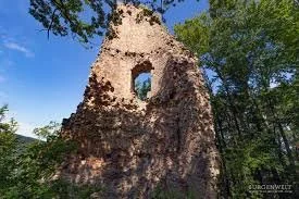 Ruined stone structure with a circular window, surrounded by trees and blue sky.
