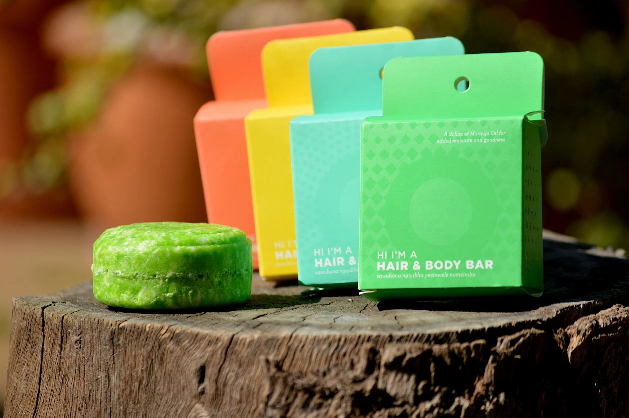 Colorful soap boxes in green, blue, yellow, and orange on a wooden surface with a green soap bar in front of them