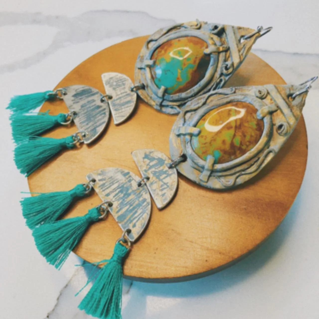 Set of jewelry including large teardrop-shaped earrings, round earrings, and butterfly-shaped earrings with turquoise tassels, displayed on a round wooden surface.