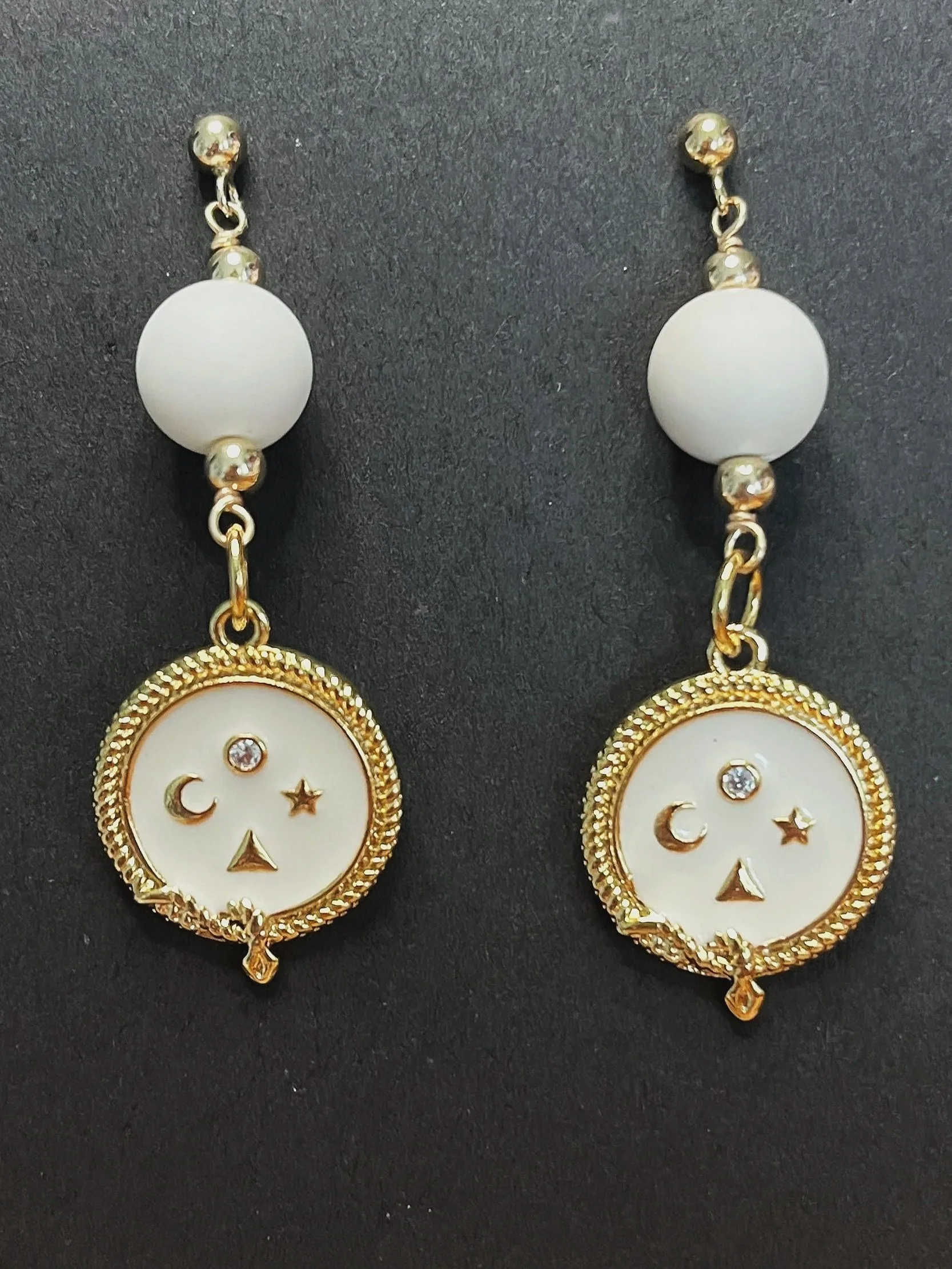 Gold and white earrings with moon, star, and triangle motifs, featuring small rhinestones.